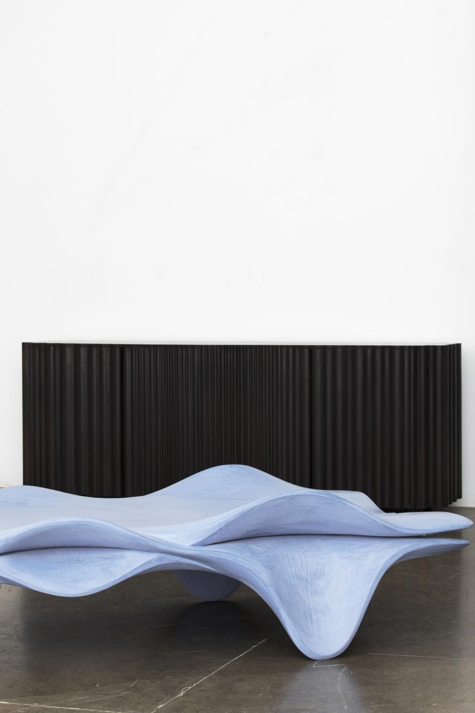 Sculptural blue furniture piece with waves, complemented by a black corrugated backdrop, showcasing modern design aesthetics.