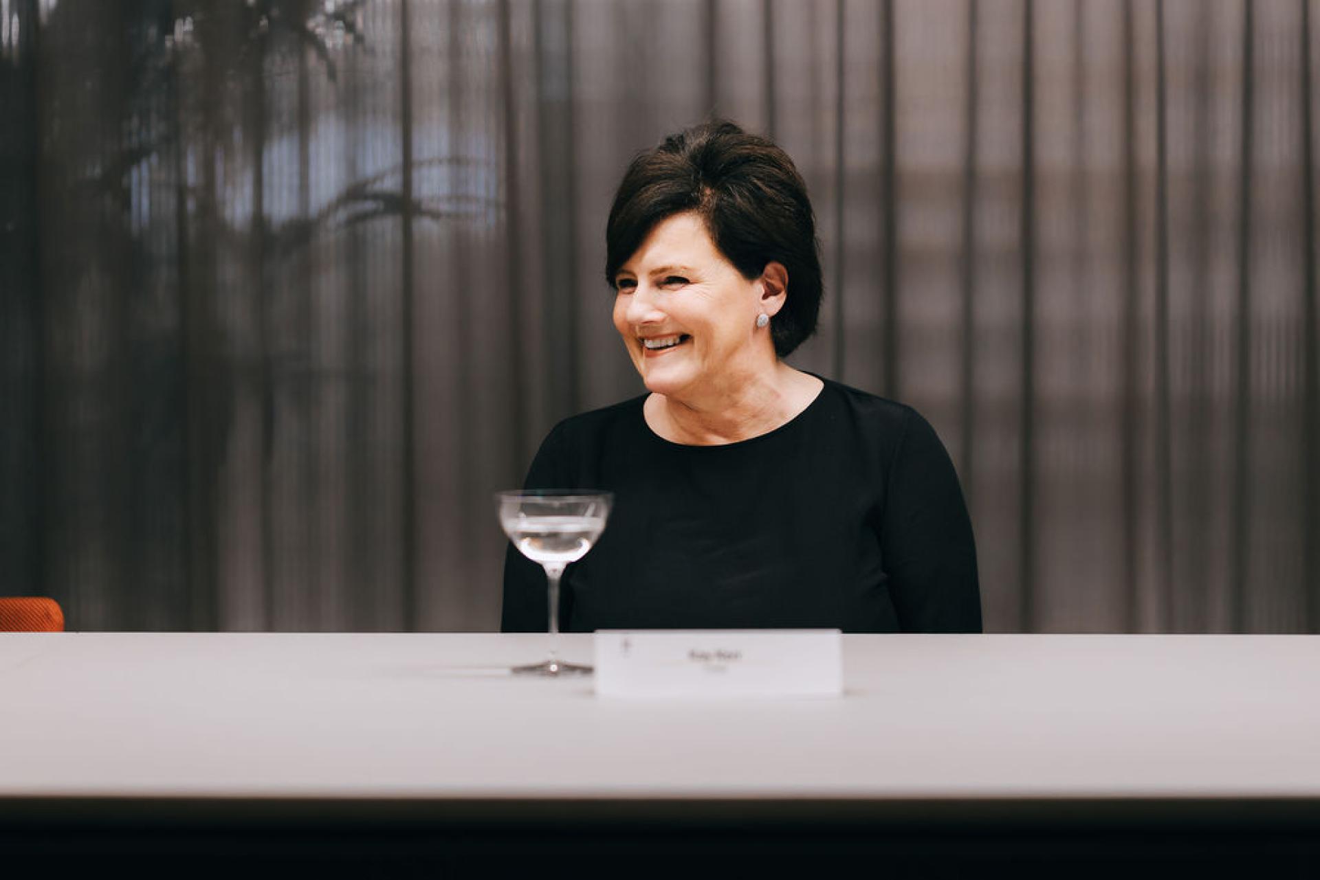 Smiling woman in a black dress seated at a table, discussing biomaterials and sustainability at an event.