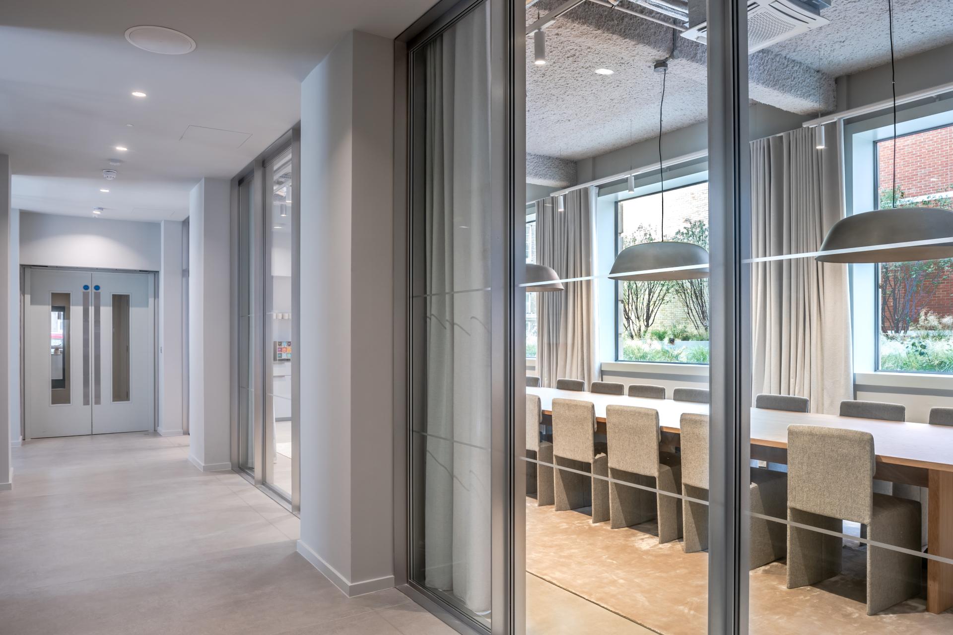 Modern workspace hallway leading to a well-lit meeting room with a large table and greenery outside.