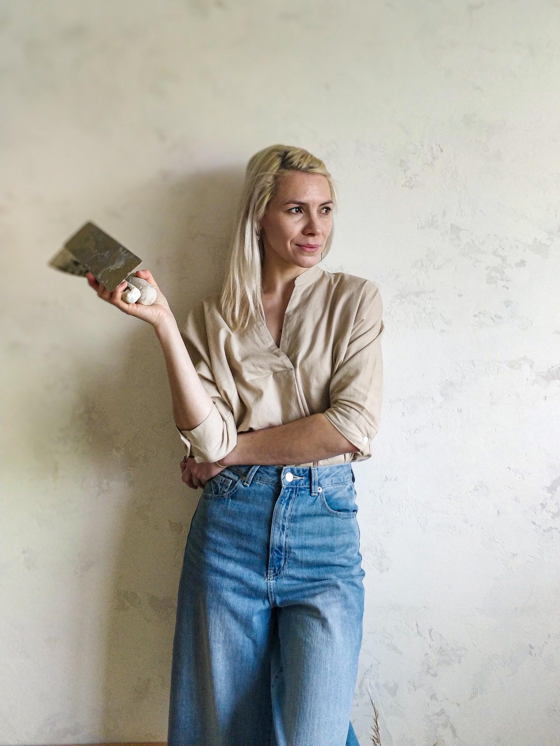 Artisan showcasing unique finishing techniques with a trowel against a textured wall, representing Vacarda Design's craftsmanship.