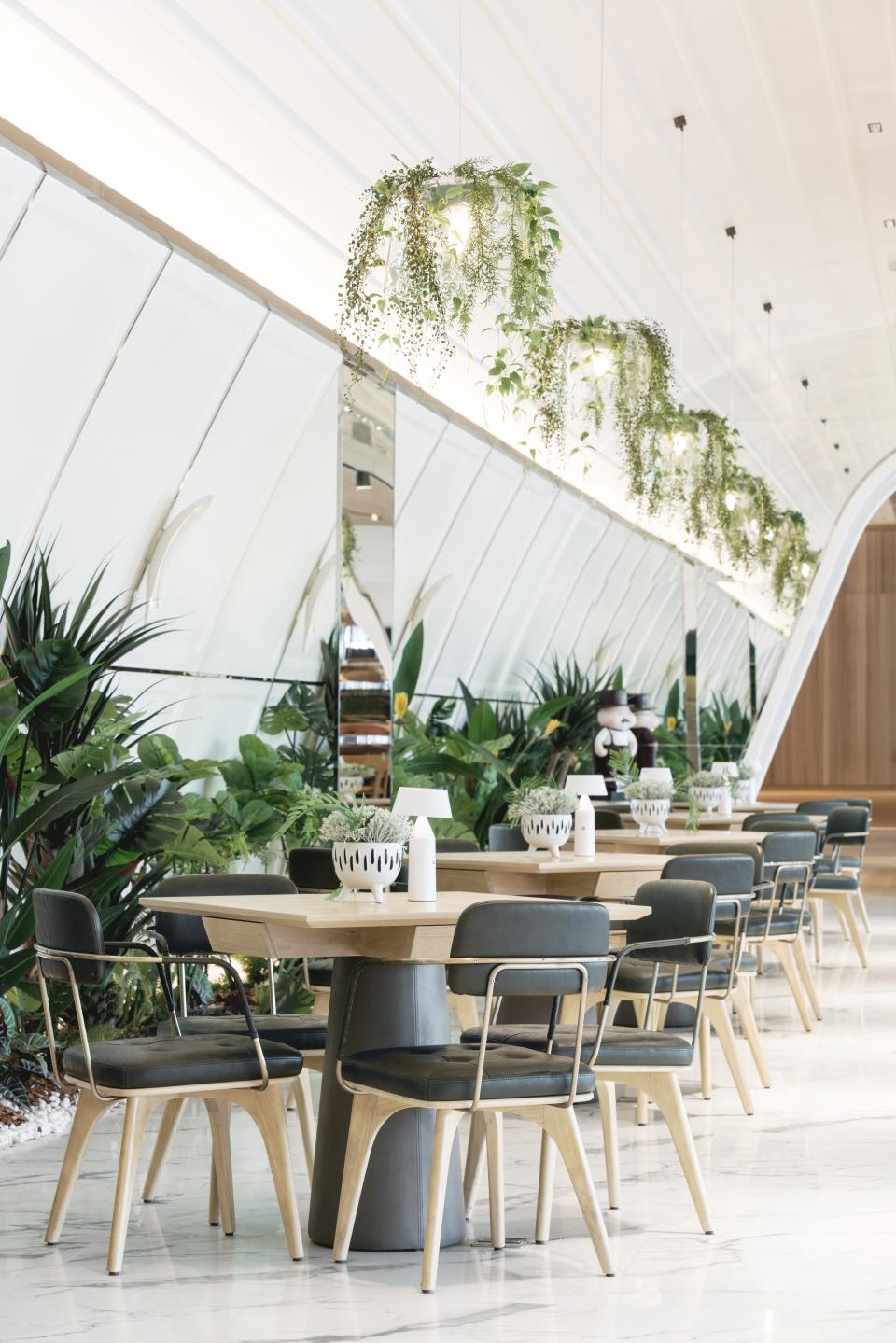 Elegant coffee shop interior featuring wooden tables, stylish chairs, and lush greenery, designed for a relaxing atmosphere.