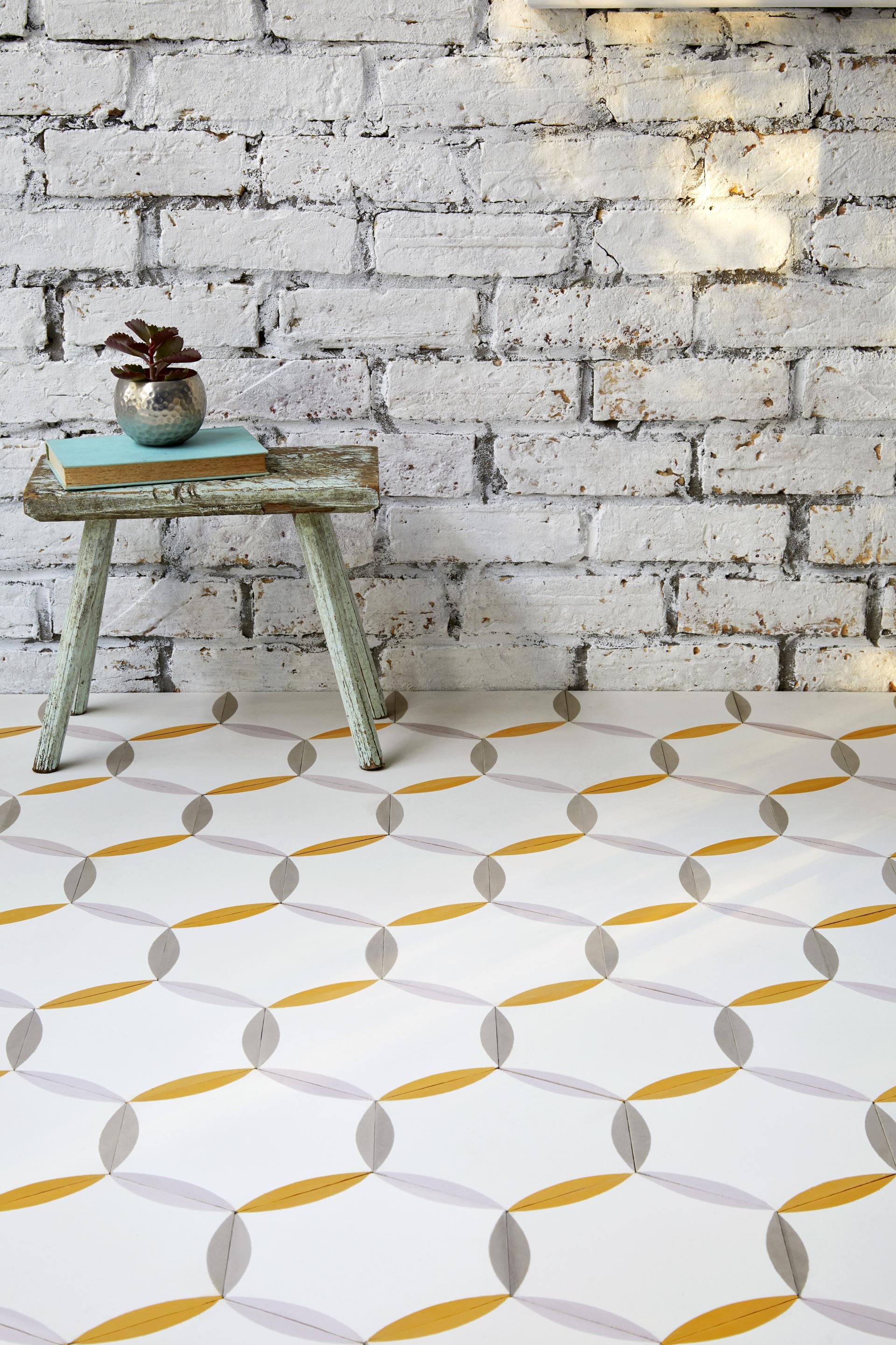 Patterned tiles from the Bermondsey collection by Lindsey Lang, featuring geometric designs in yellow and gray against a brick wall.