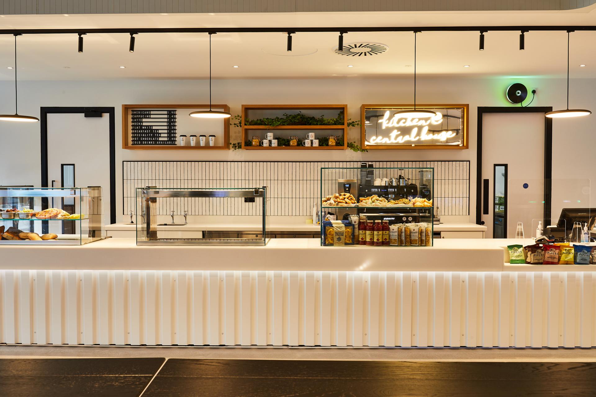 Modern café interior at Central House, showcasing a sleek serving counter, pastry display, and decorative neon sign.