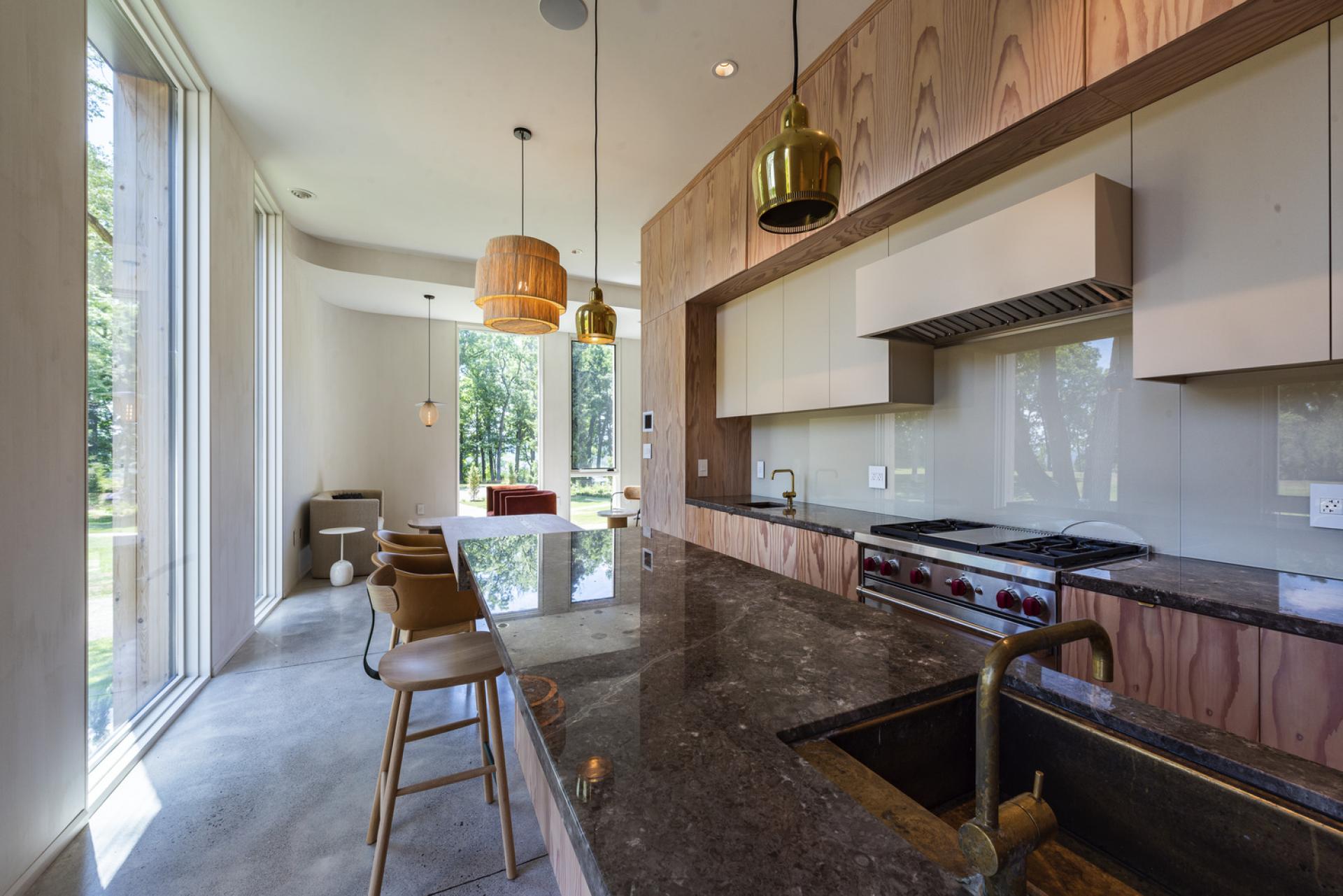 Modern kitchen interior in Fold House, featuring sleek cabinetry, a granite countertop, and large windows overlooking nature.