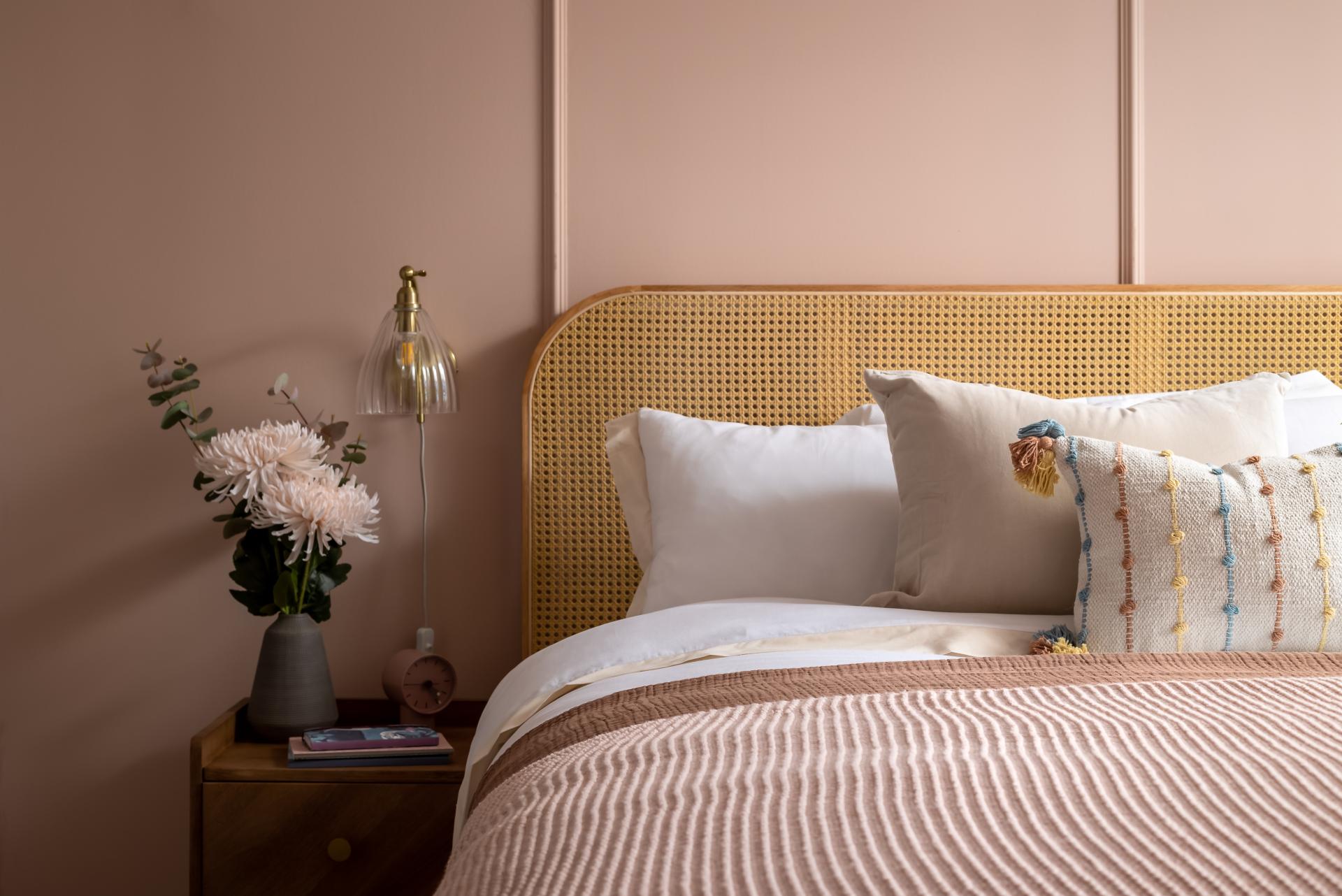 Stylishly decorated bed with a woven headboard, plush pillows, and decorative flowers, showcasing modern interior design.