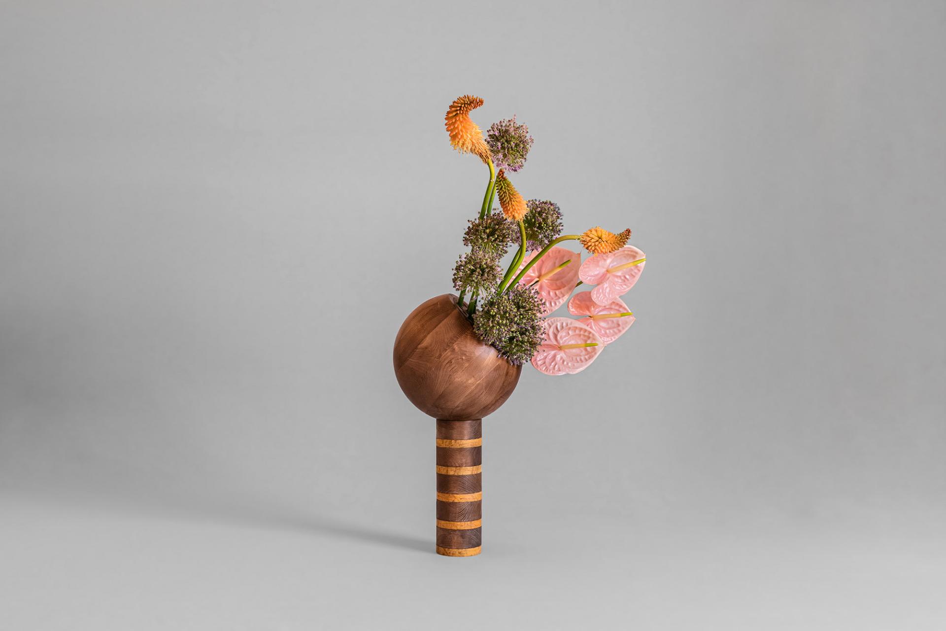 Sculptural floral arrangement featuring a wooden base, showcasing vibrant anthuriums and unique textured plants, highlighting Masquespacio's design vision.
