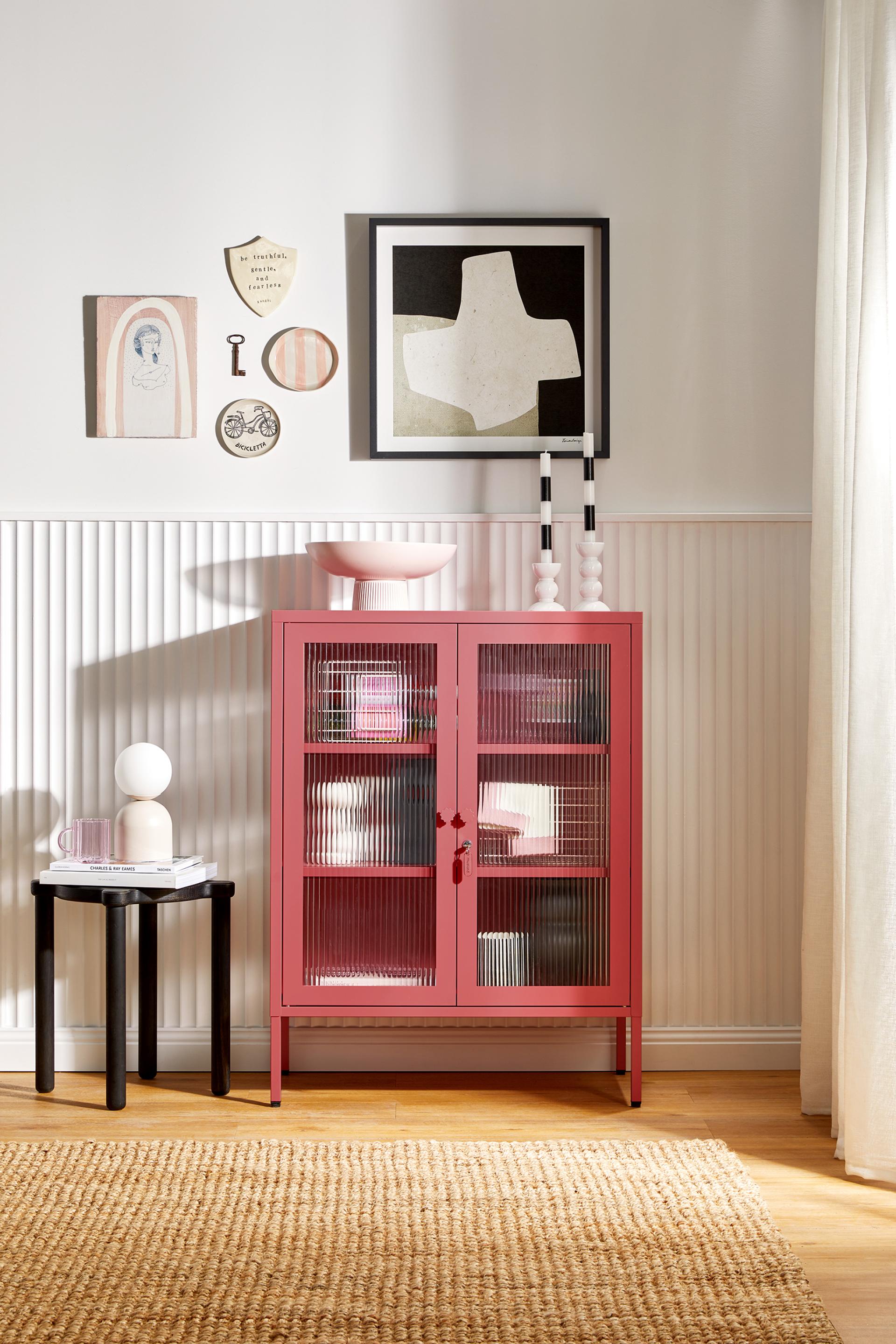 Stylish pink cabinet from Mustard Made's Glass Collection, featuring playful design and decorative wall art in a bright room.