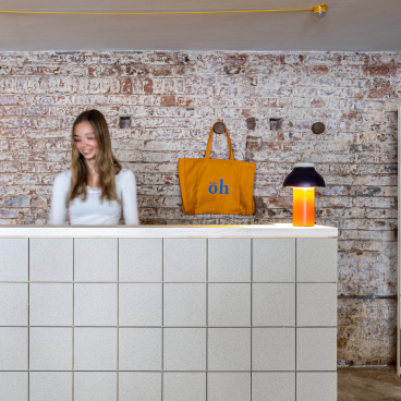 Modern retail space featuring a warm welcome desk, decorative lamp, and a stylish tote bag against a rustic brick backdrop.