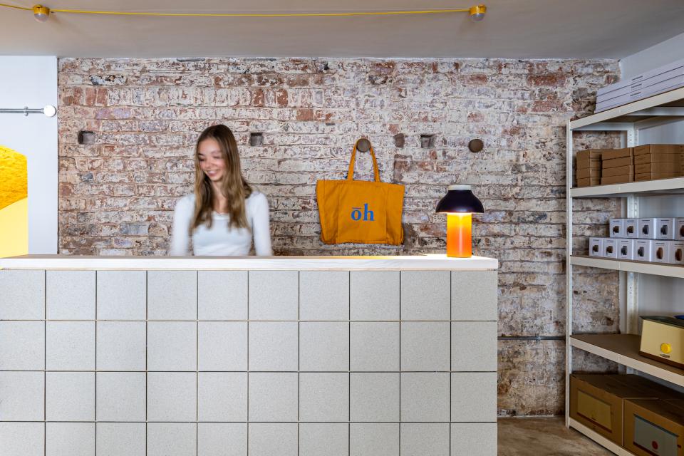 Modern retail space featuring a warm welcome desk, decorative lamp, and a stylish tote bag against a rustic brick backdrop.
