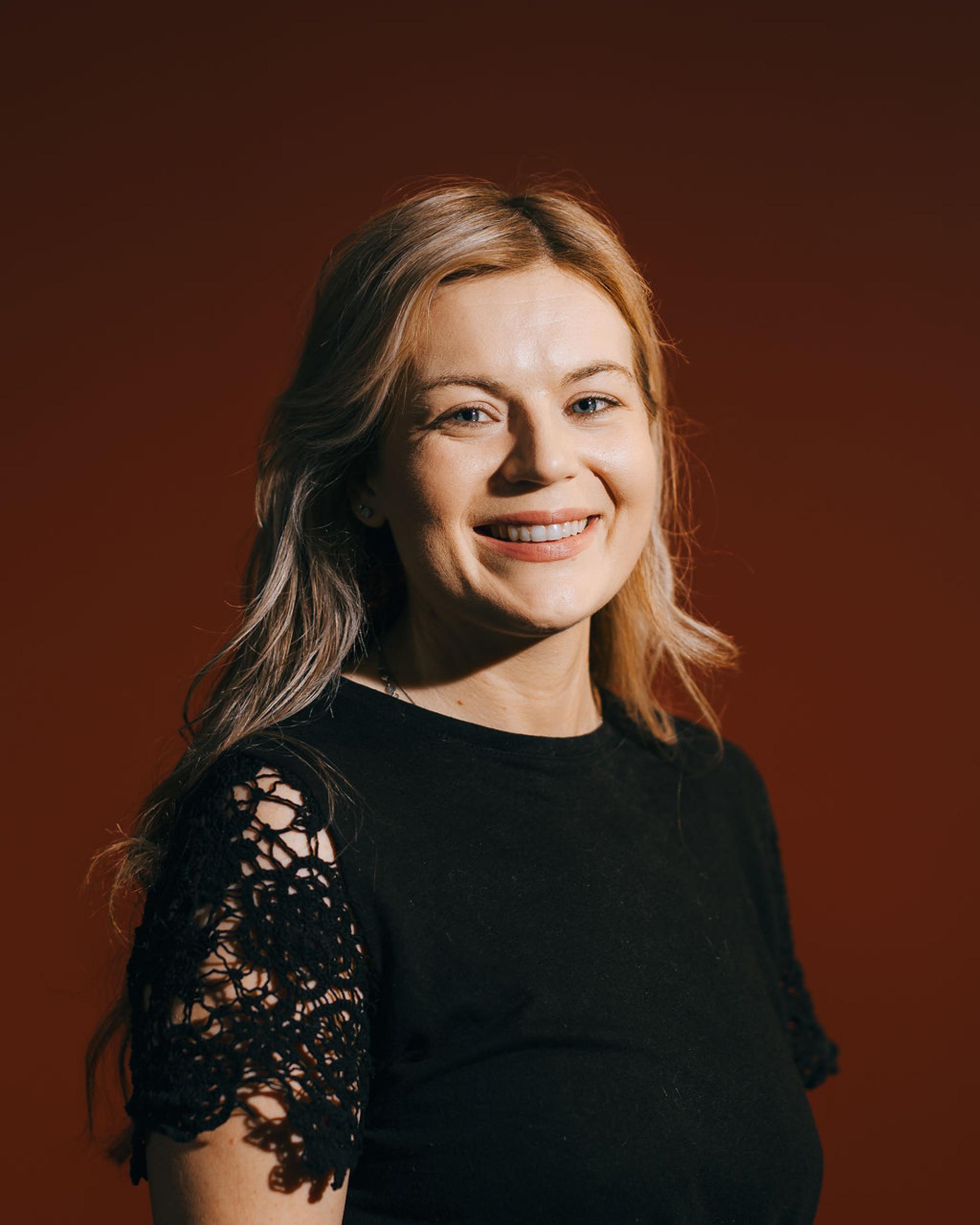 Smiling woman in a black shirt with lace sleeves, representing conversations about sustainability and biomaterials in the article.