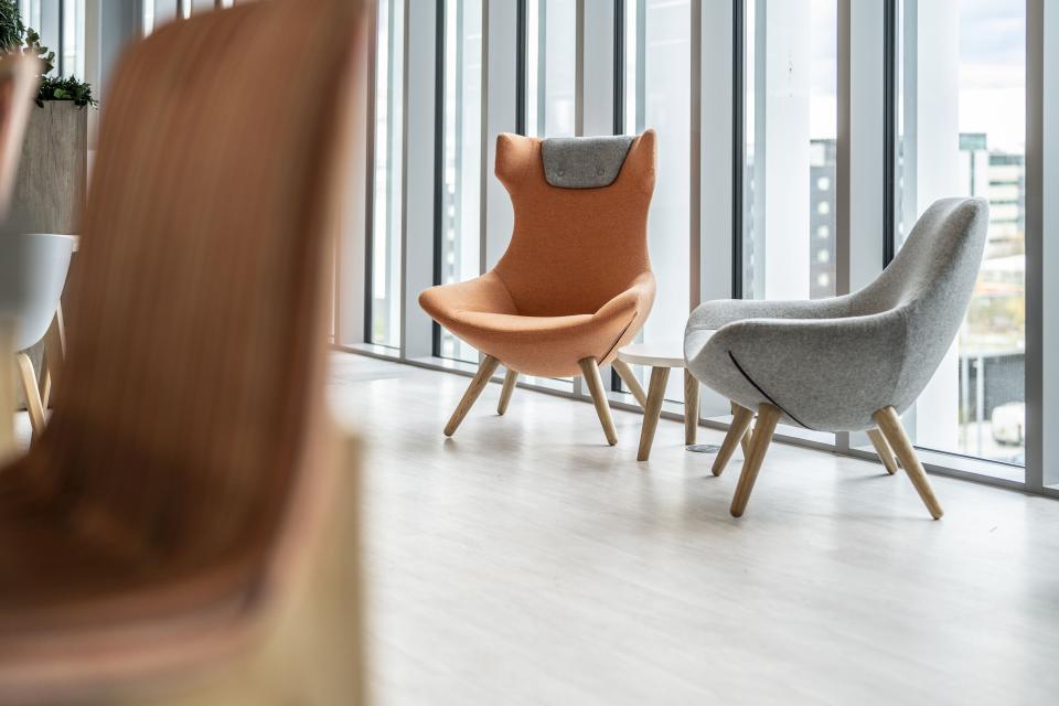 Stylish orange and gray chairs with wooden legs in a modern office space, highlighting flexible furniture design.
