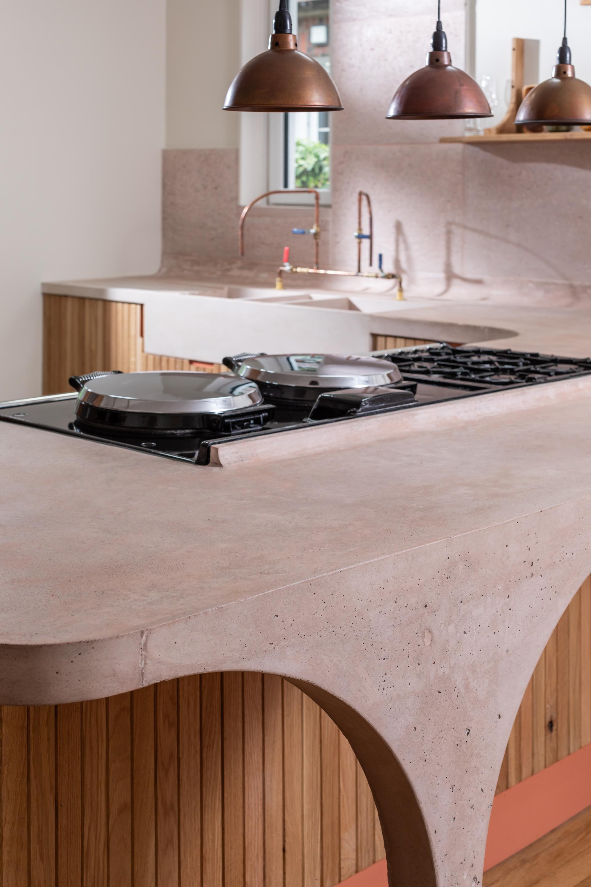 Curved pink concrete kitchen countertop with Scottish Oak cabinetry and stylish copper pendant lights in a modern design.