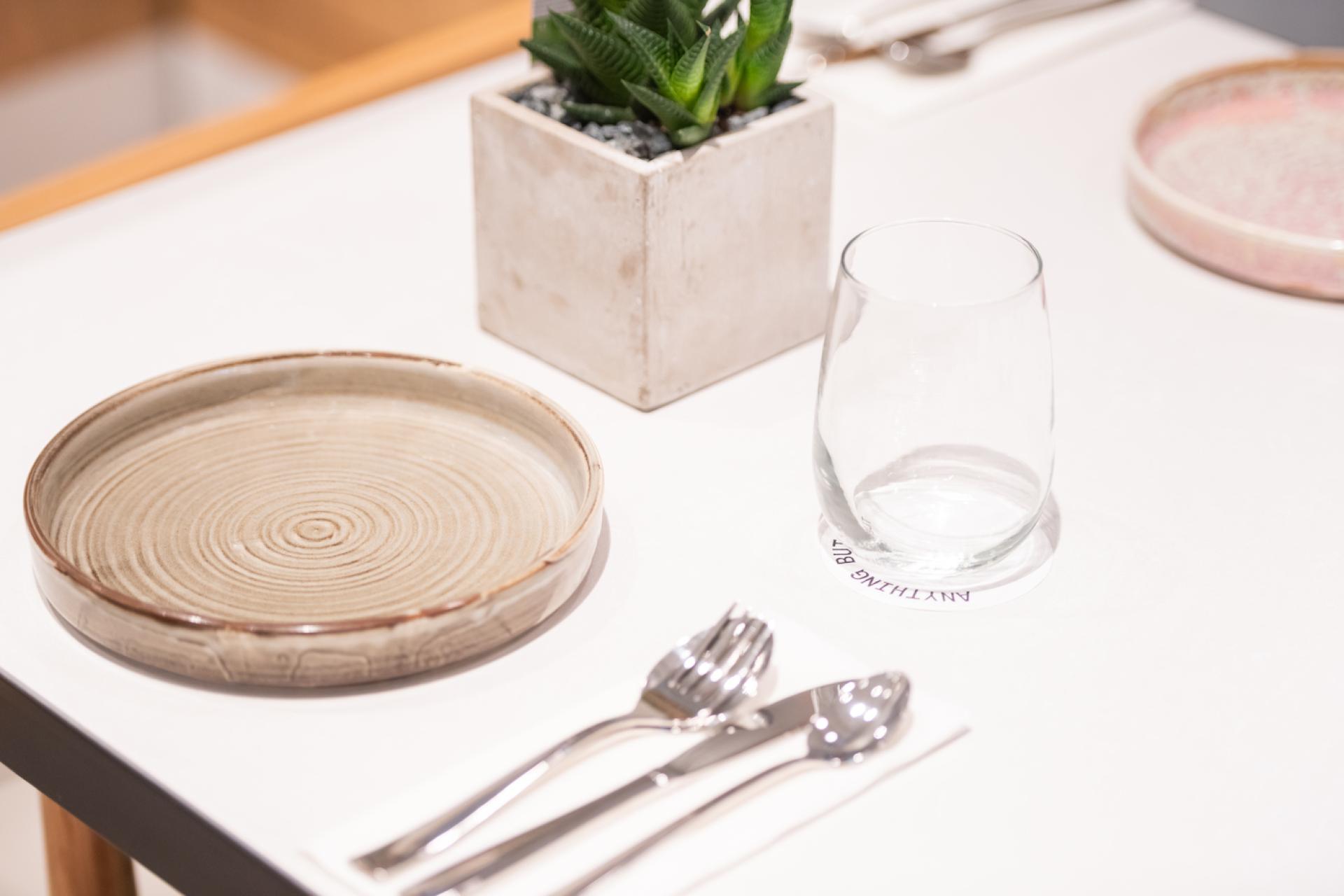 Elegant table setting featuring a handcrafted plate, glass, cutlery, and decorative plant for a dessert experience.