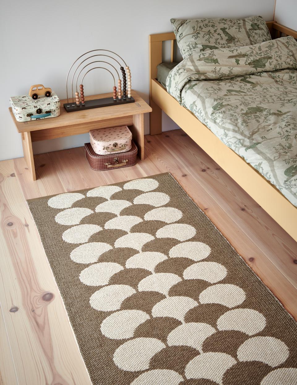 Stylish Swedish rug made from BIOVYN™, featuring a unique circular pattern, enhances a cozy bedroom setting.