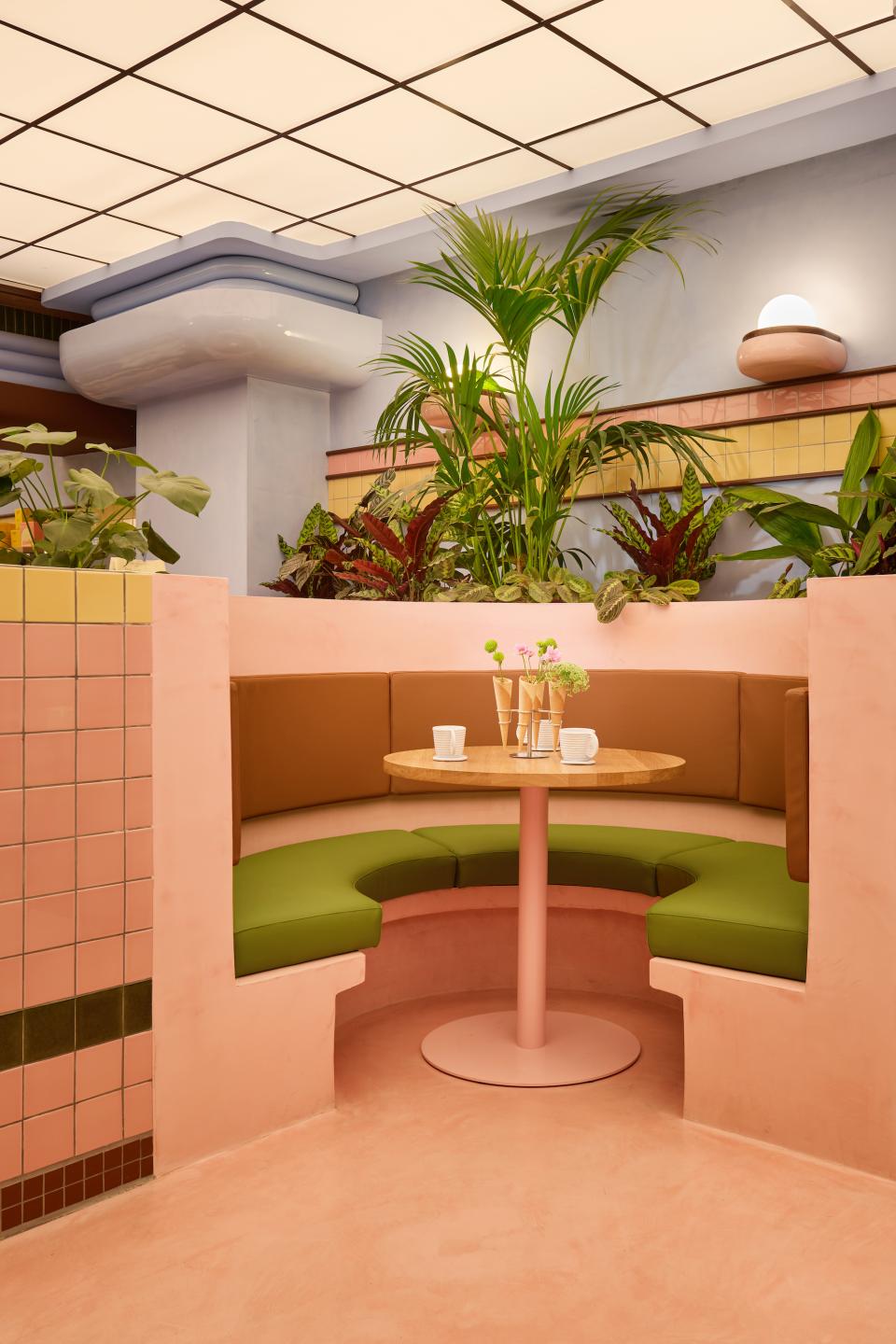 Vibrant Art Deco-inspired ice cream parlour seating area featuring a round wooden table surrounded by lush greenery.
