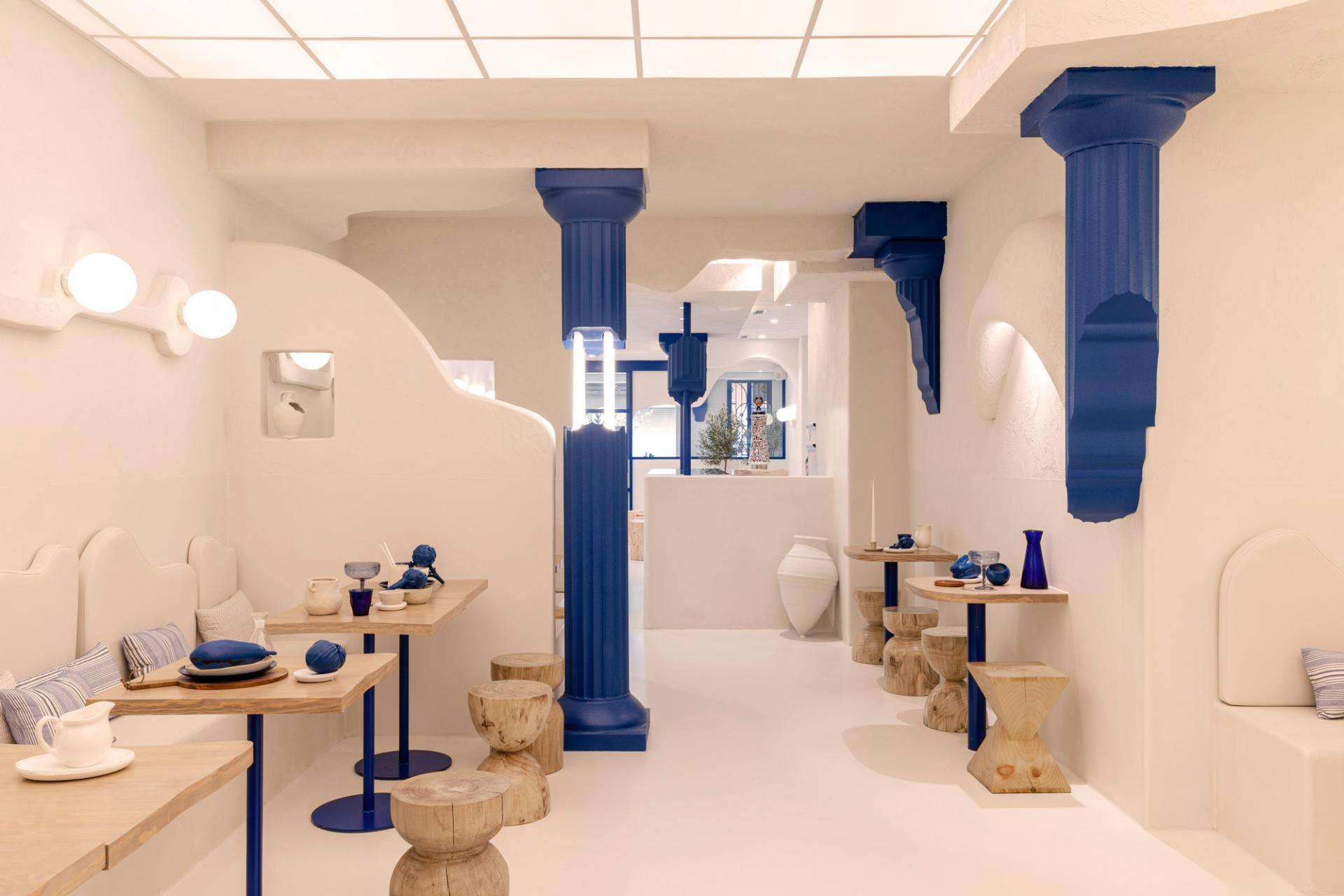 Modern Greek restaurant Egeo features minimalist decor with white walls, blue columns, and wooden tables, reflecting a blend of tradition and technology.
