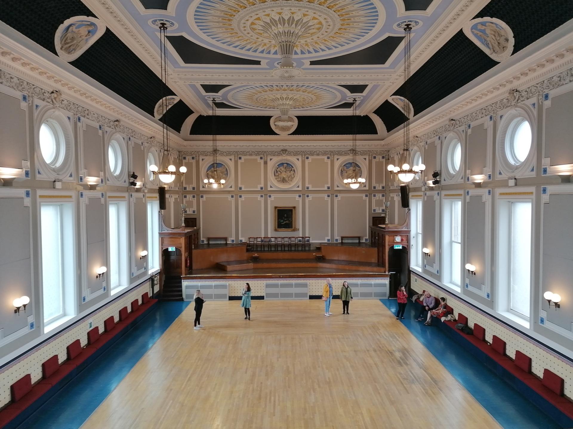 Refurbished ballroom at Todmorden Town Hall featuring elegant decor, wooden floor, and visitors enjoying the space.