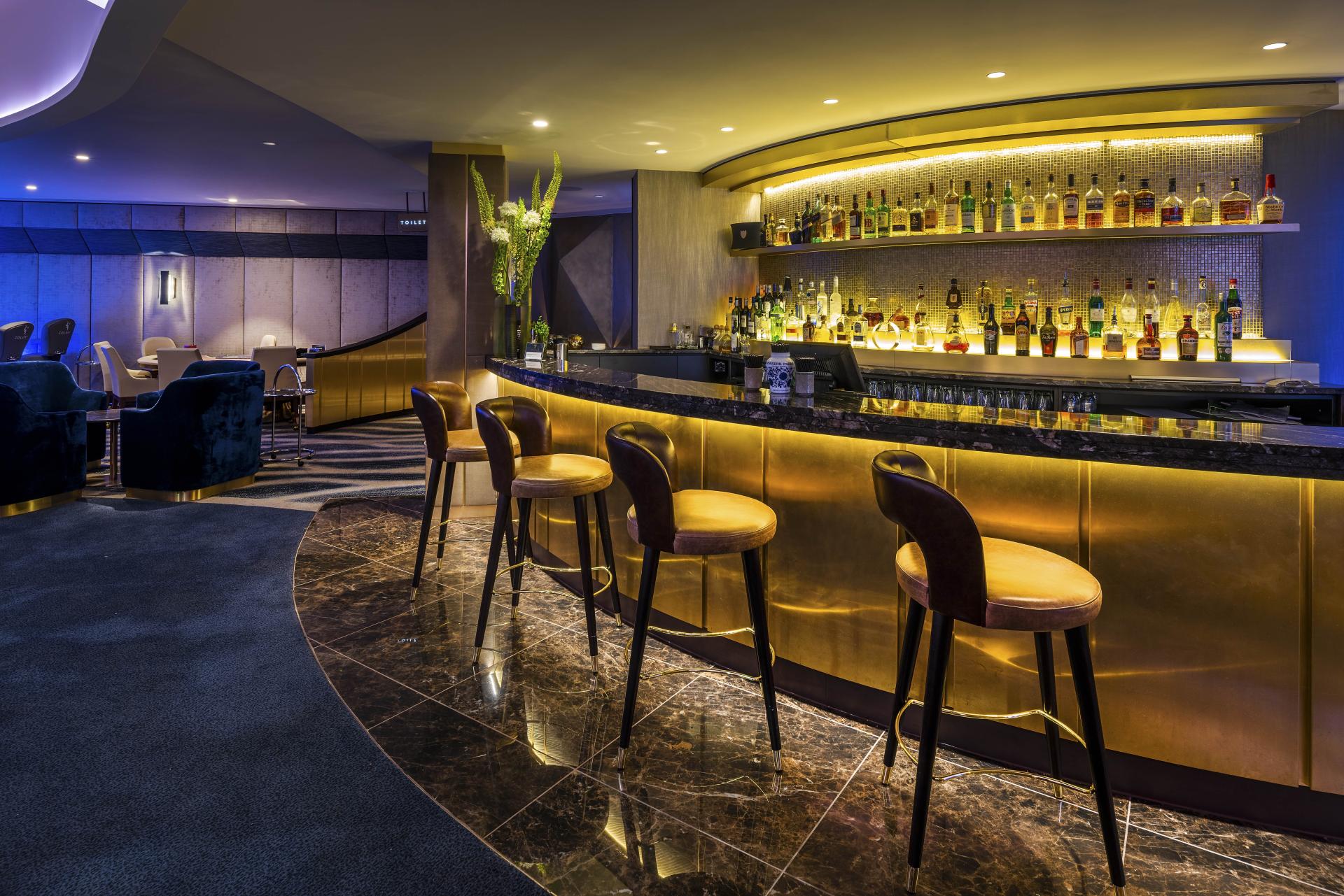 Stylish bar area at The Colony Club, featuring elegant seating, a shimmering backlit shelf, and a chic atmosphere.