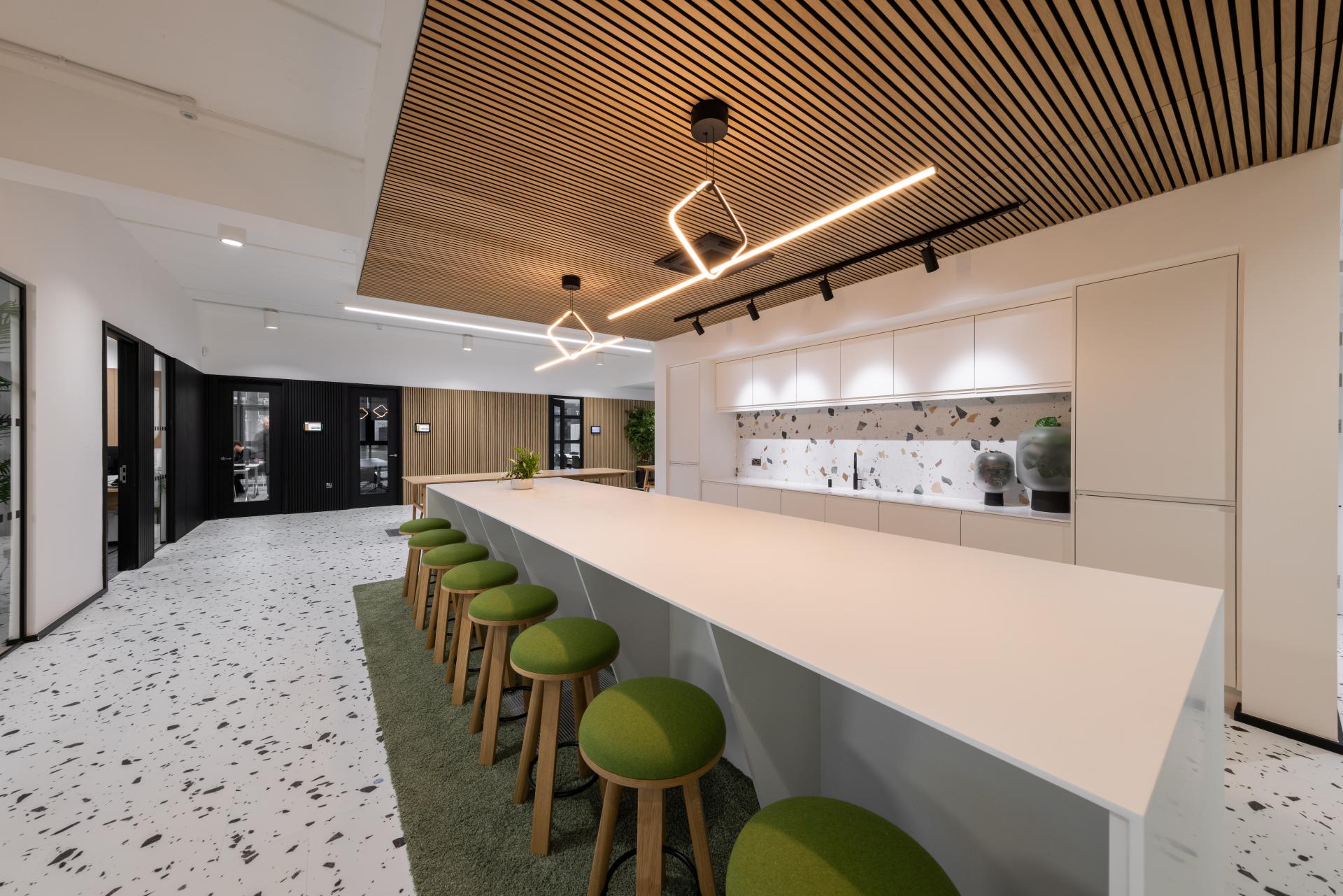 Modern interior featuring white terrazzo flooring, sleek cabinetry, and vibrant green stools in a biophilic design workspace.
