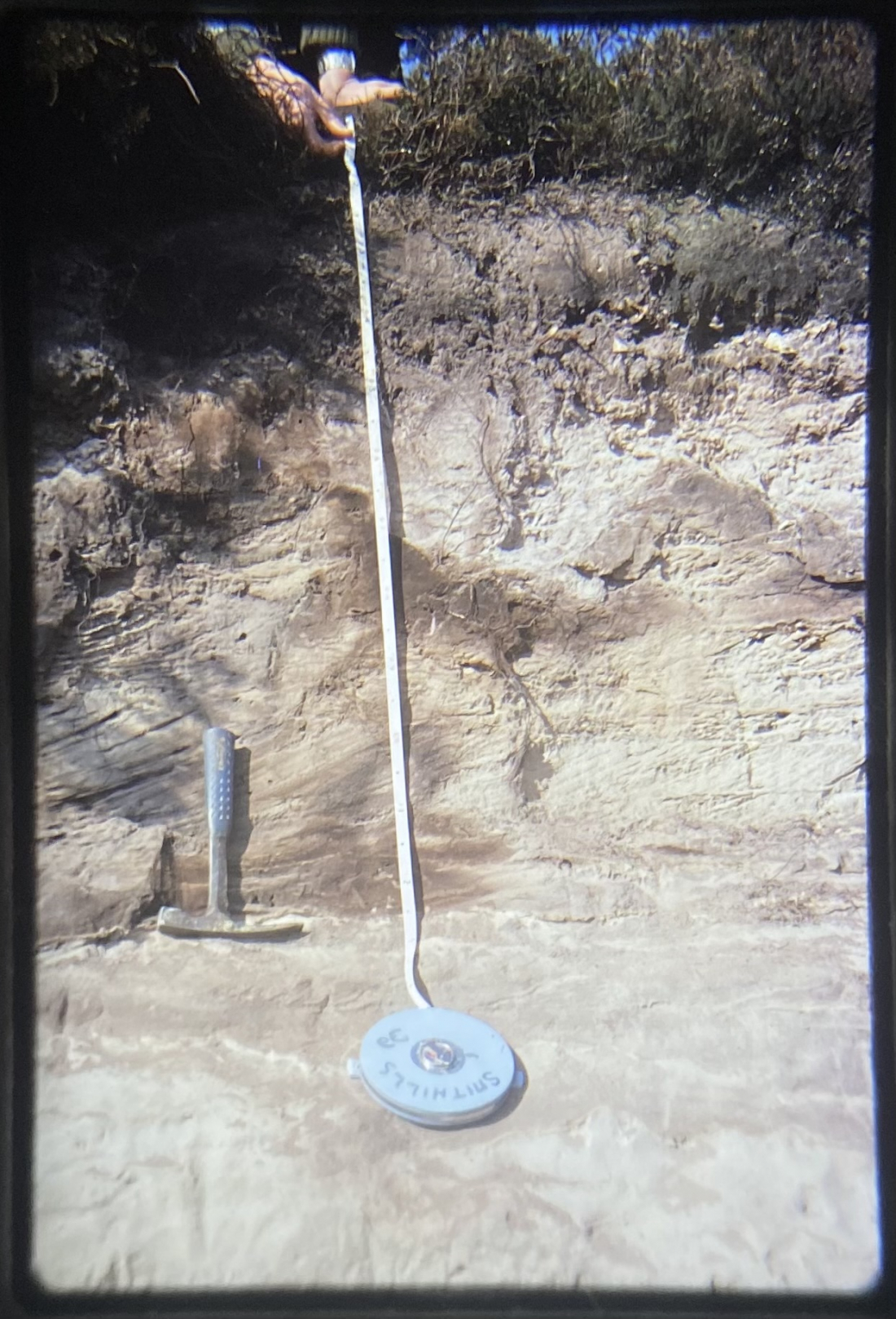 The Tape Measure (1963): An image from 1963 from Georgie’s Grandfather's photo archive: a geology field trip to Dorset, featuring a tape measure and pickaxe, measuring earth layers. Shot on film.