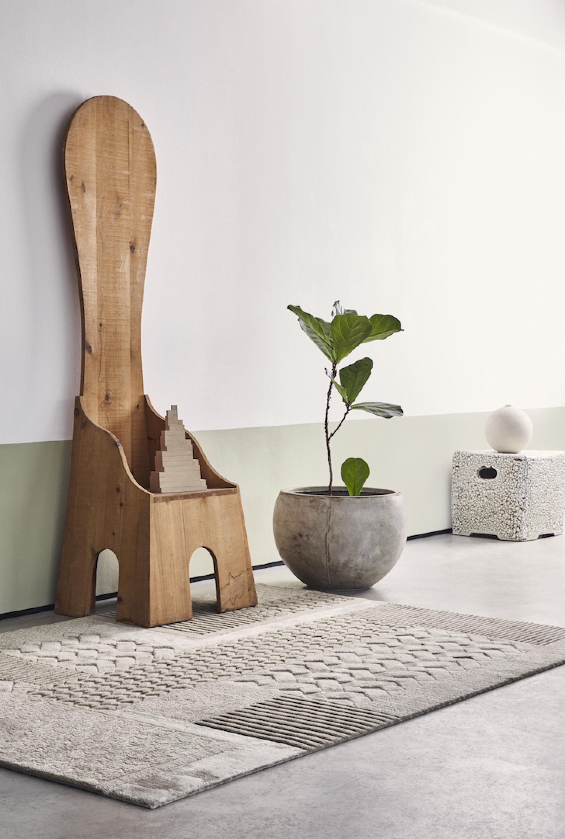 Eclectic living space featuring a unique wooden chair, a textured rug, and a stylish potted plant.