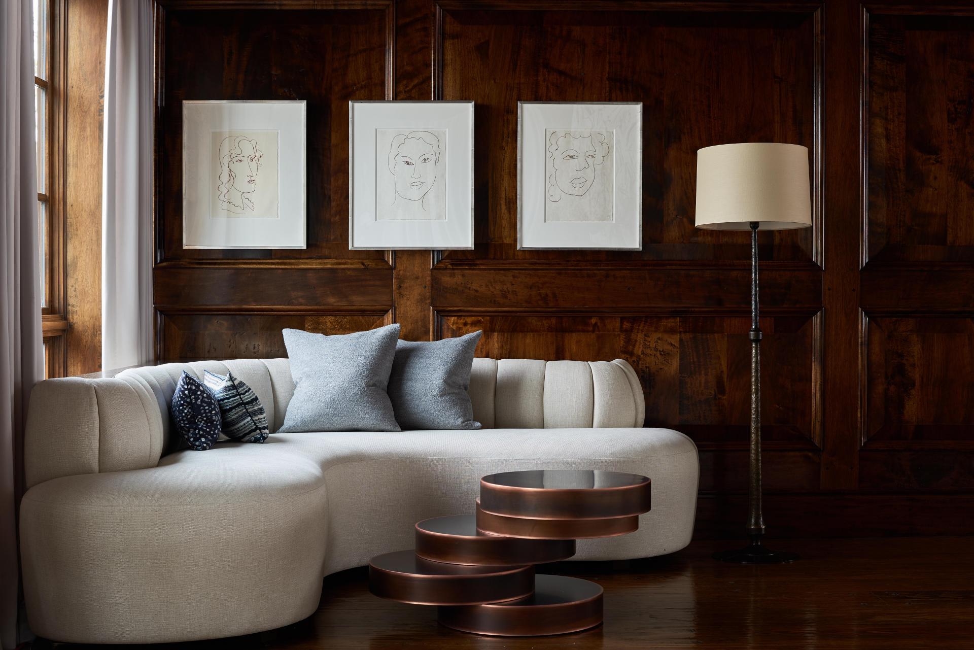 Elegant modern chalet living room with a curved sofa, art pieces, and a stylish lamp, showcasing luxury design.