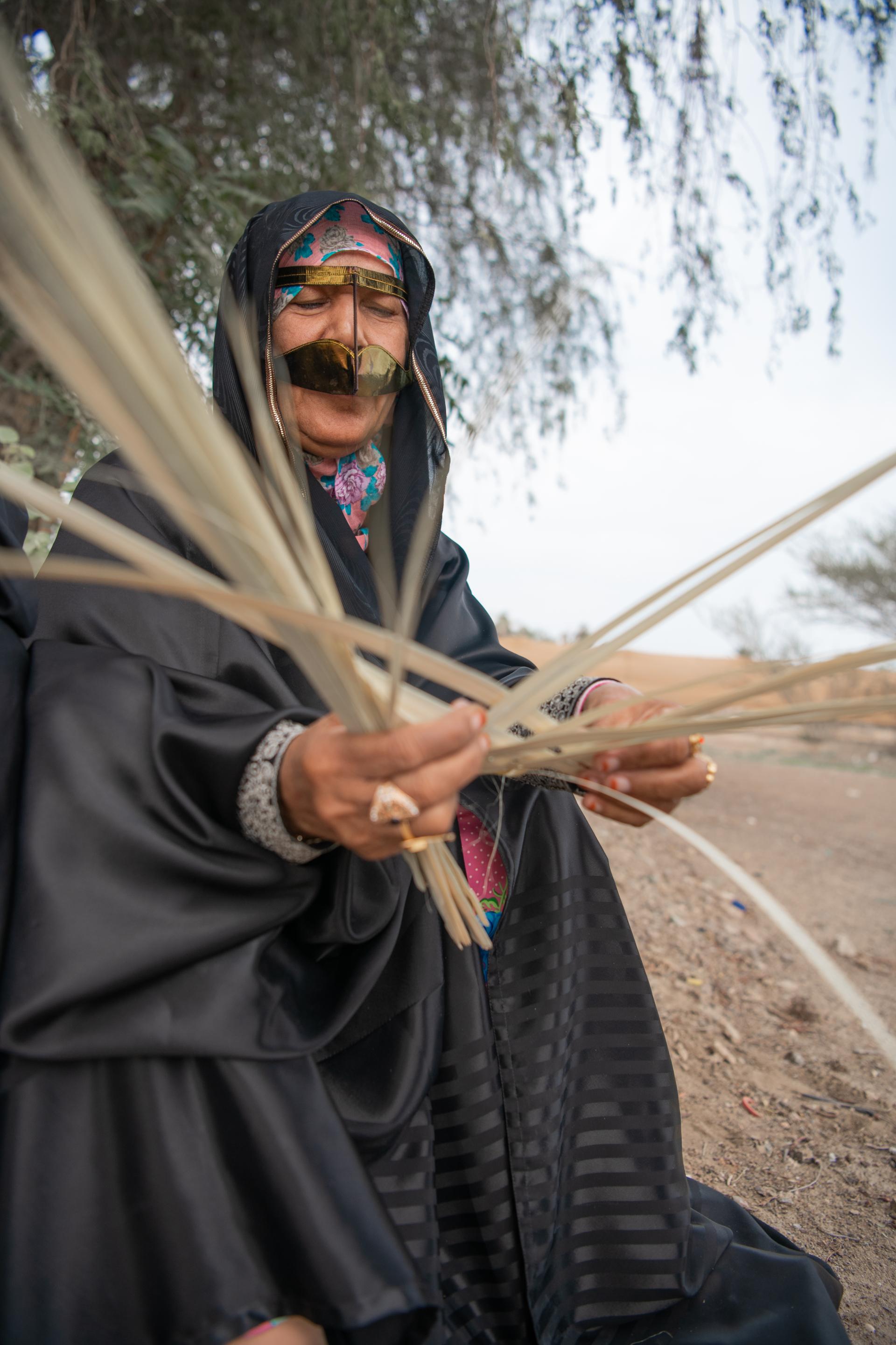 Woman in traditional attire weaving palm fronds, showcasing craftsmanship and cultural heritage at Irthi Contemporary Crafts Council event.