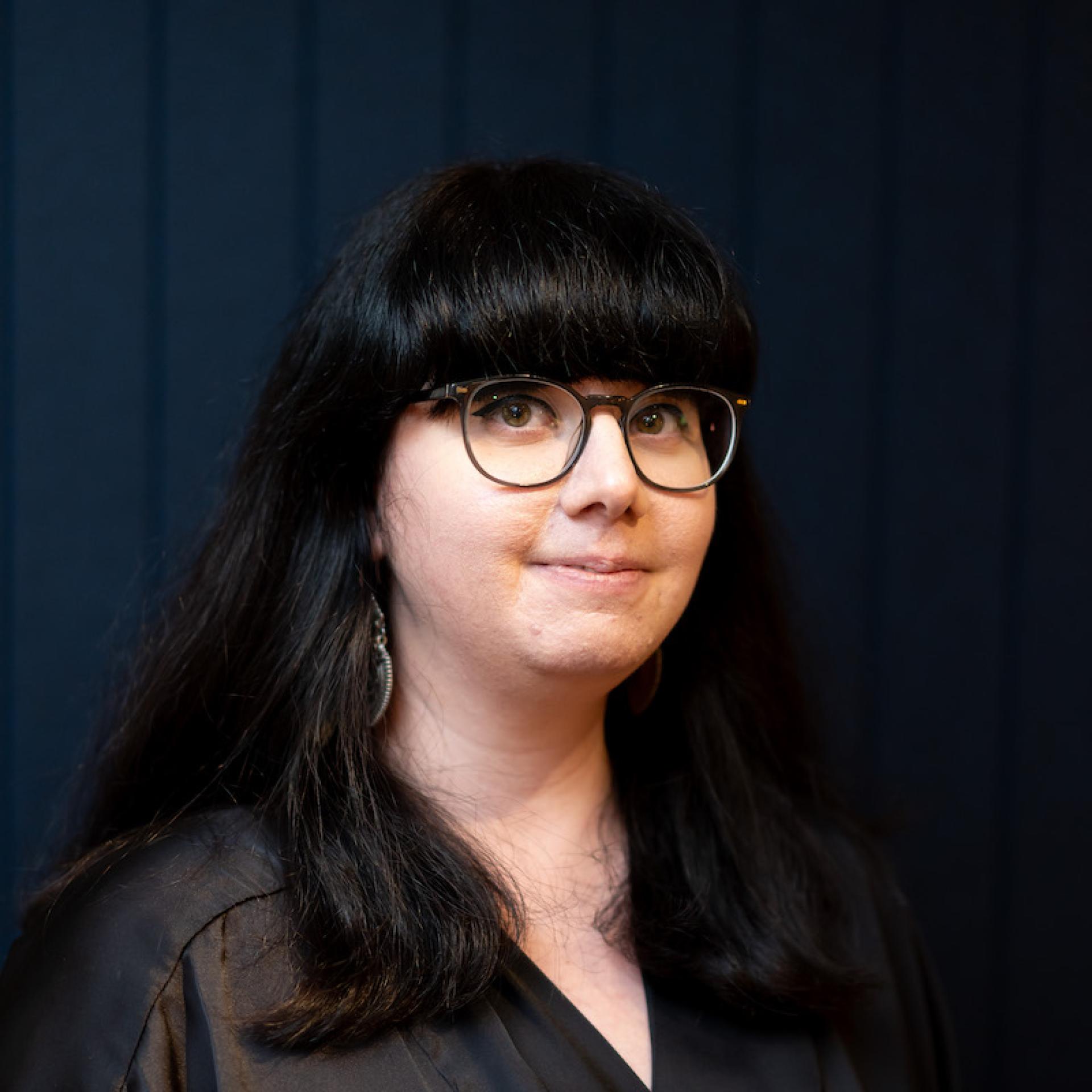 Professional woman with long dark hair and glasses, reflecting modern workplace diversity and collaboration.