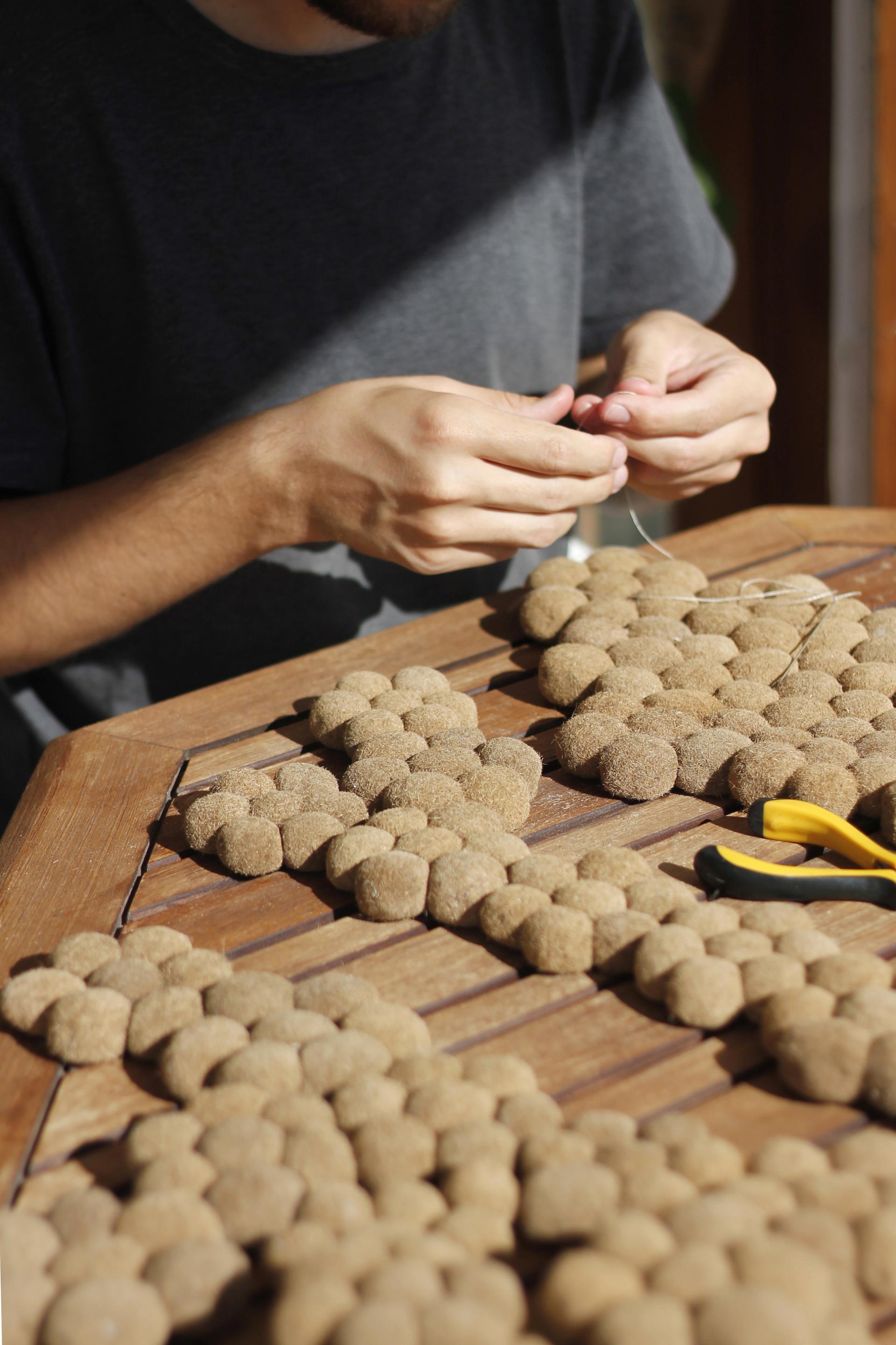 Craftsperson assembling natural Posidonia sea grass components into a textile design on a wooden table.