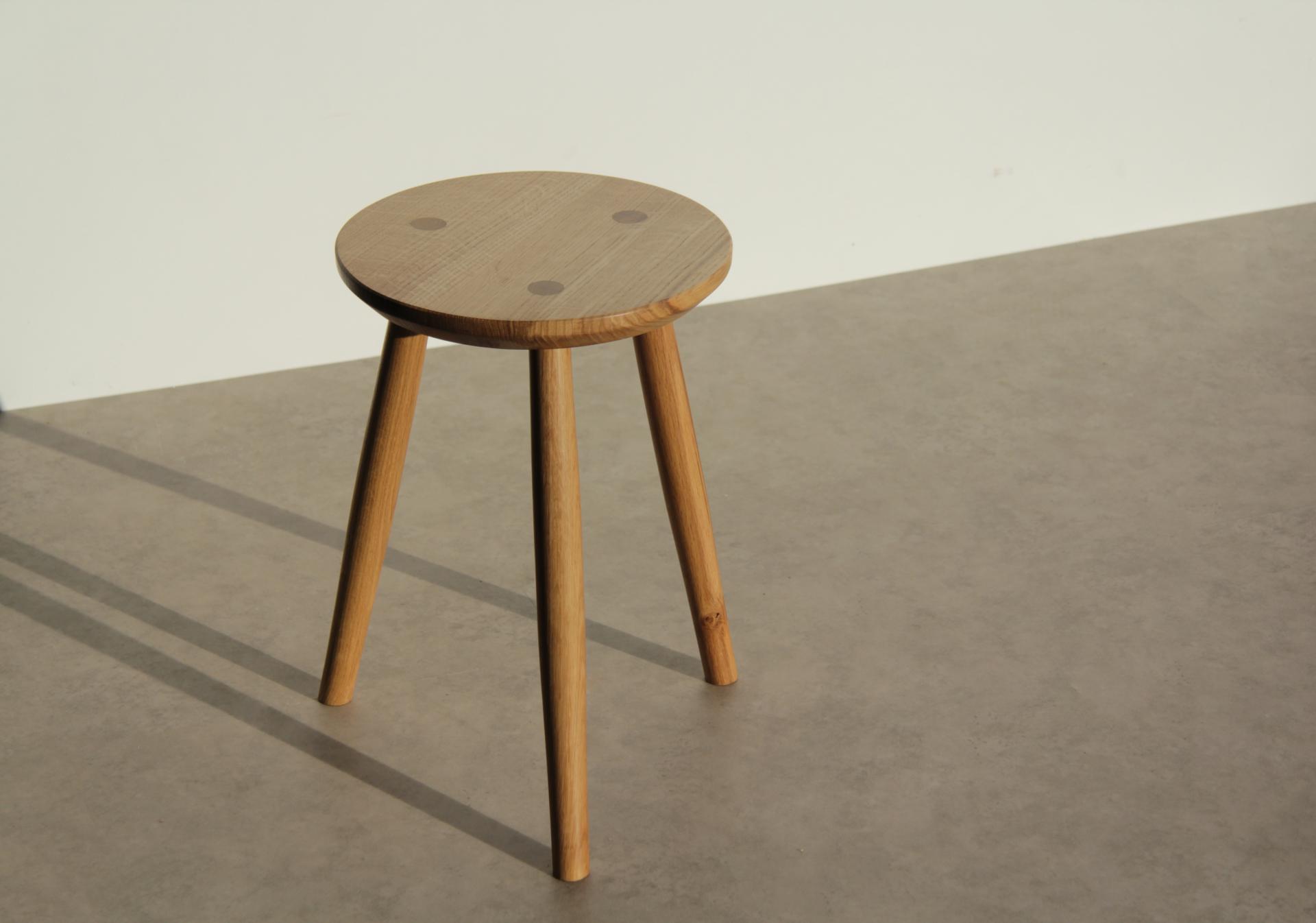 Minimalist wooden stool with three legs and a rounded top, showcasing craftsmanship in contemporary furniture design.