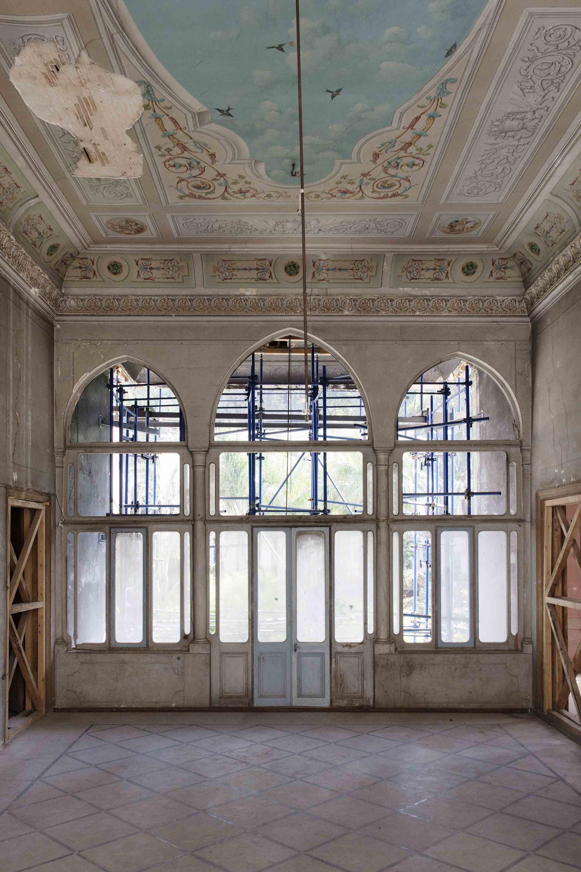 Renovated interior of a 19th-century Lebanese house, showcasing intricate ceiling details and arched windows with scaffolding.