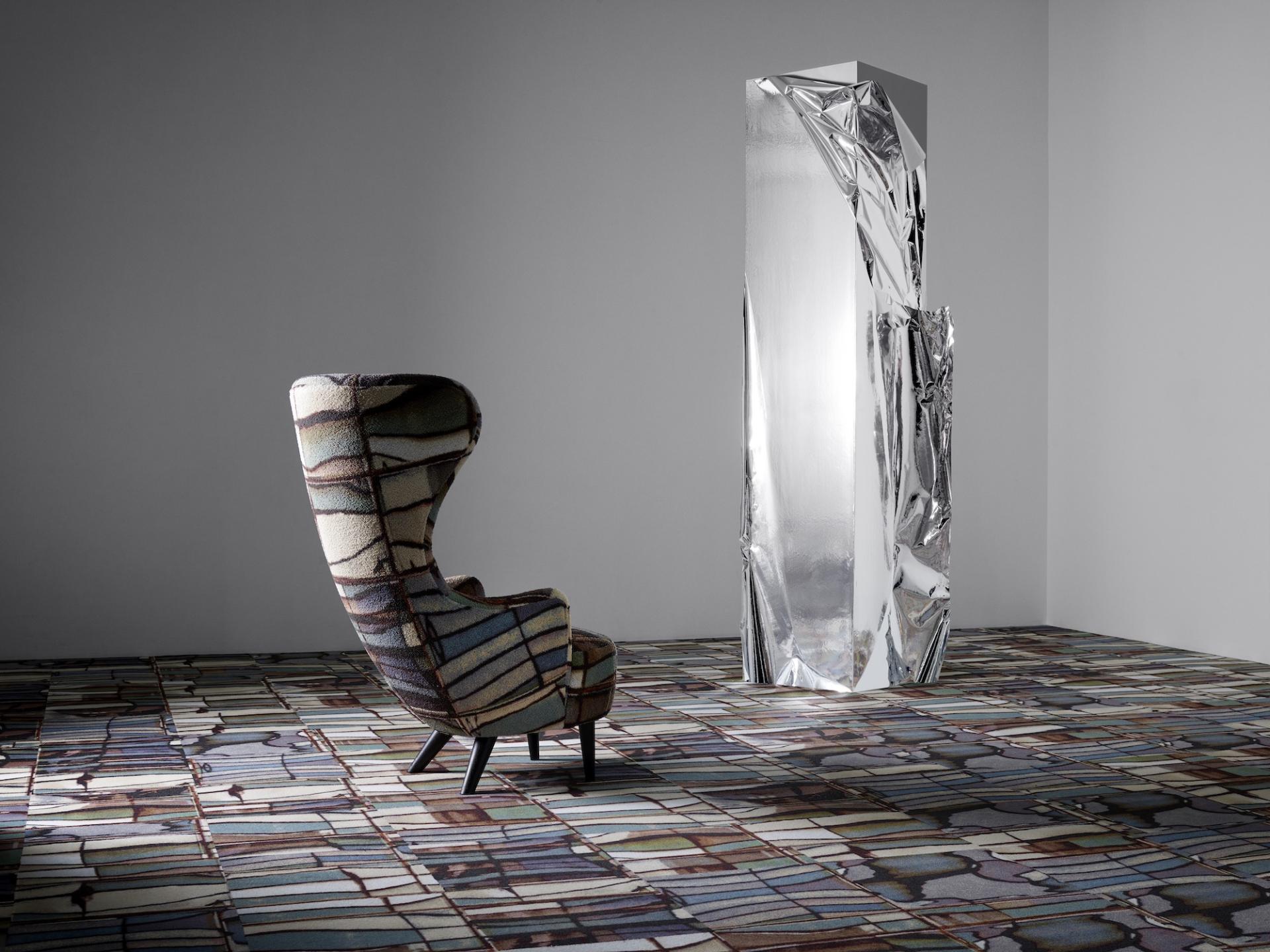 Stylish patterned chair and reflective sculpture displayed on a textured floor, showcasing innovative design in minimalist interior space.