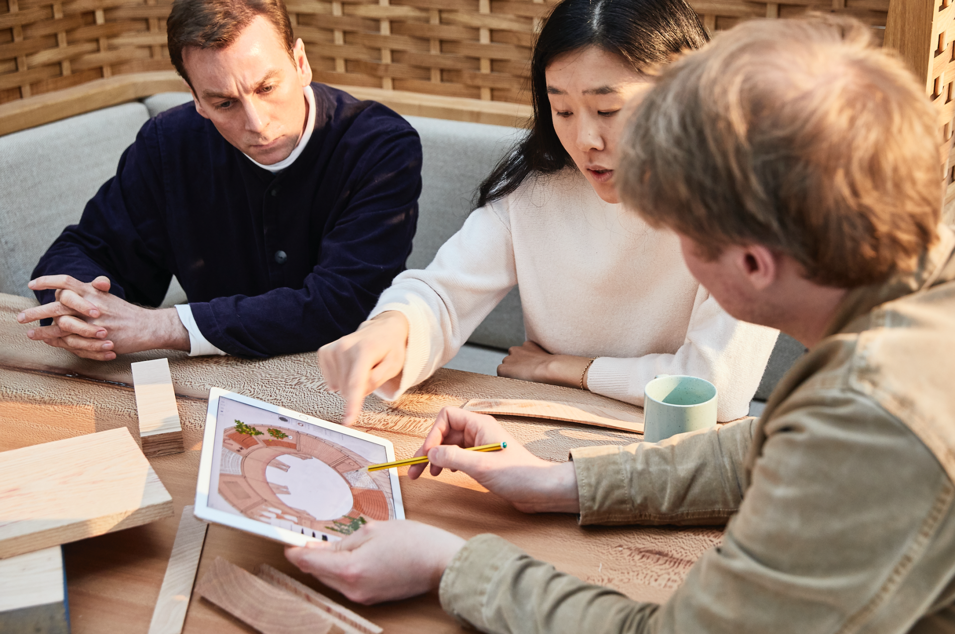 Designers discussing a red oak bar project during Milan Design Week, with sketches and wood samples on the table.