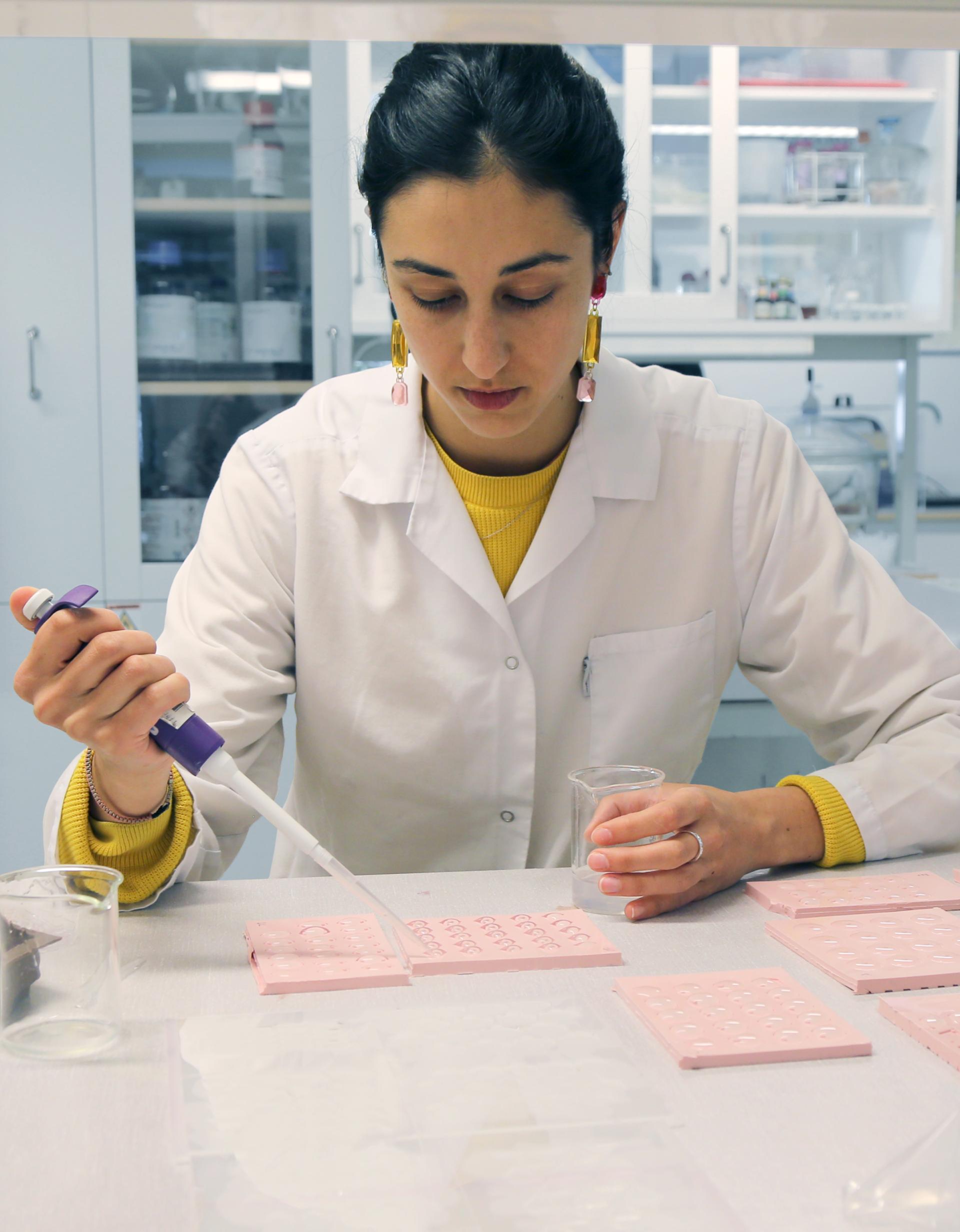 Researcher in a lab working with bio-based materials and sequins, using a pipette and glassware on a table.