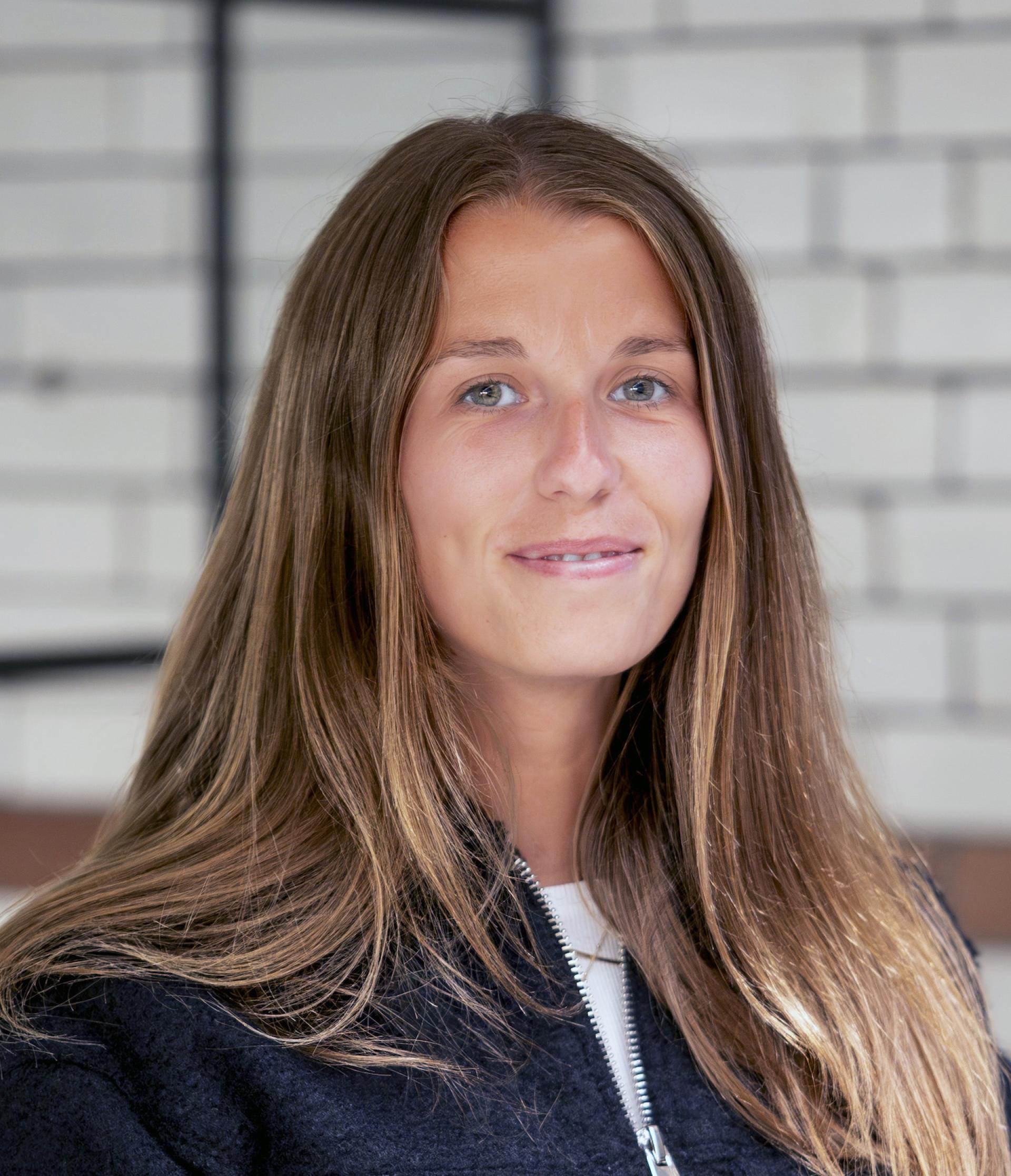 Young woman with long hair smiling, set against a modern architectural backdrop, reflecting Manchester's evolving residential landscape.