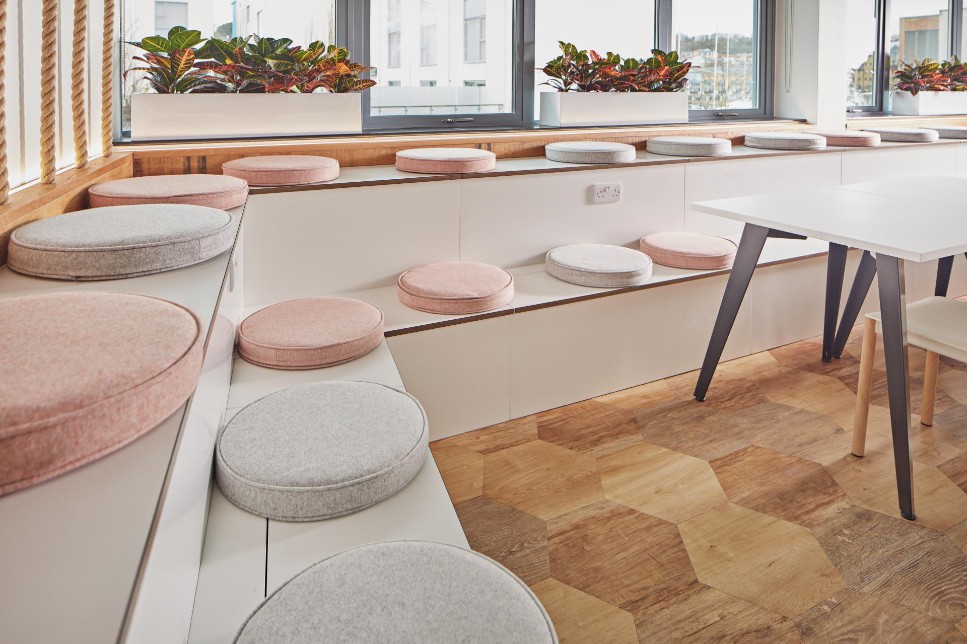 A modern workspace featuring colorful cushioned seating and a sleek table, emphasizing the workplace-hospitality design concept.