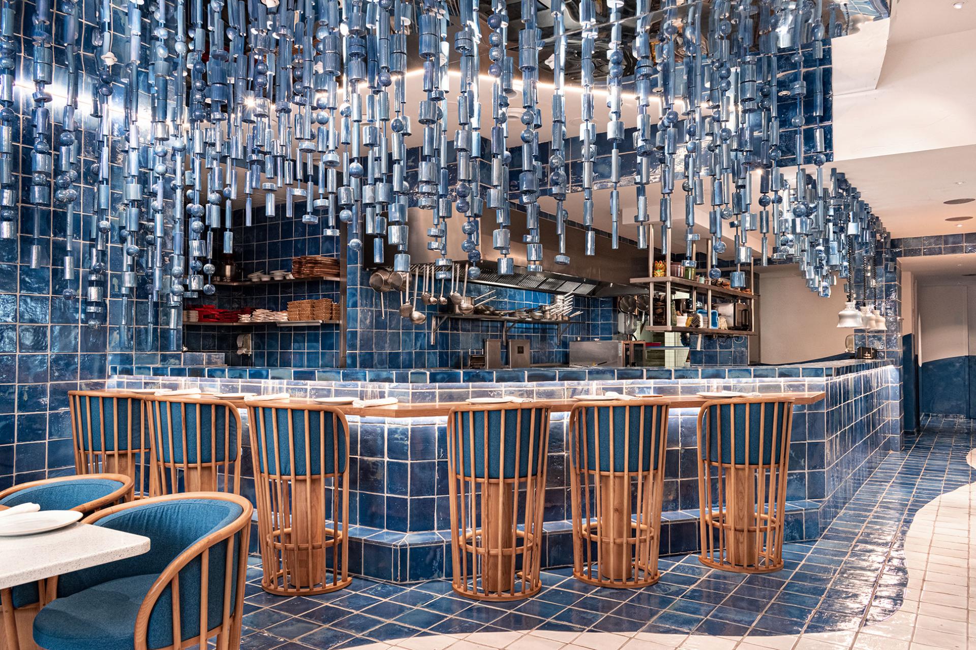 Elegant blue-tiled interior of La Sastrería restaurant, featuring unique hanging light fixtures and modern wooden seating.