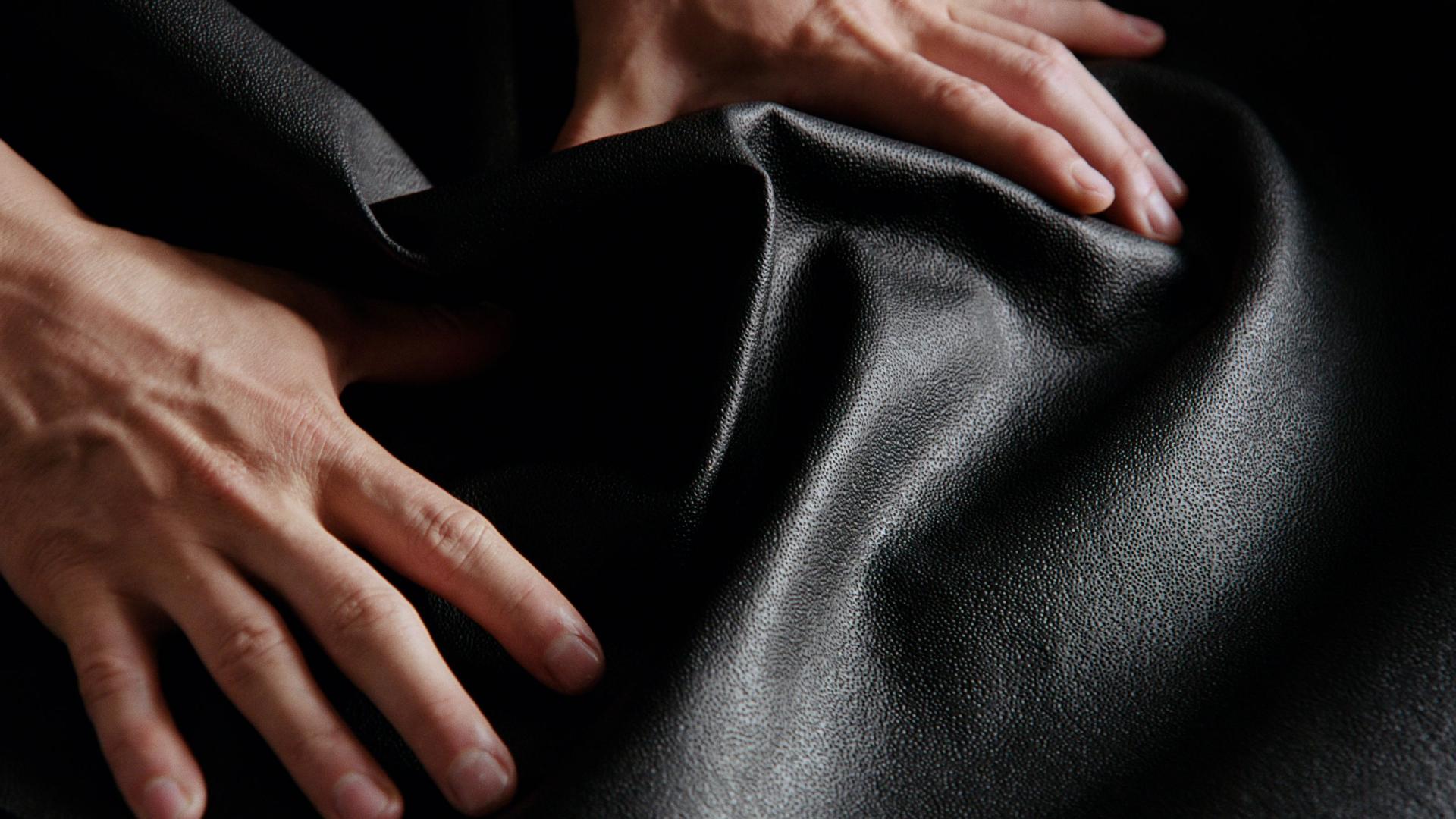 Hands gently touching a sleek, black biomaterial fabric, highlighting innovative, low-carbon textile solutions.
