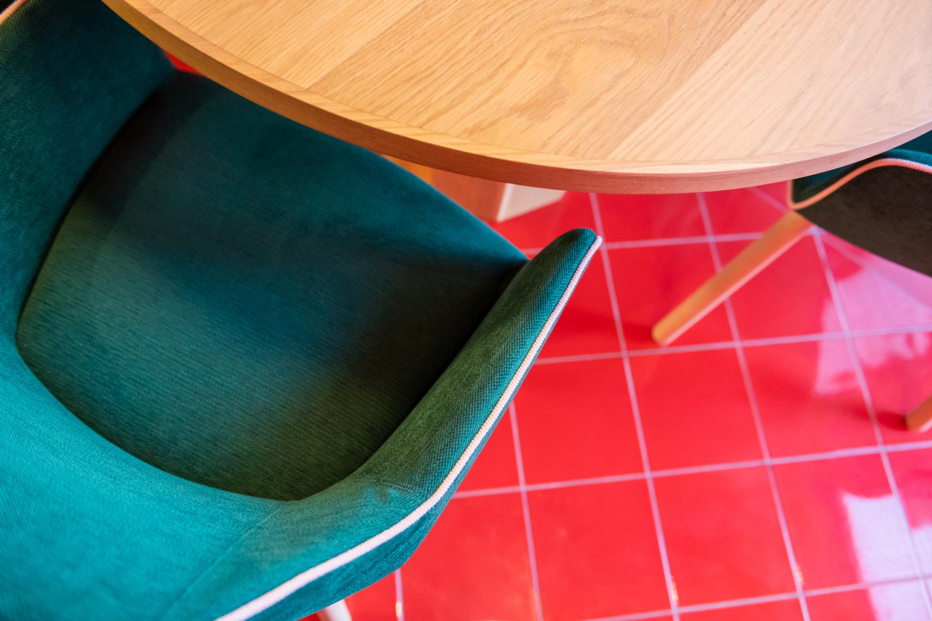 Stylish green upholstered chair with a wooden table, set against vibrant red tiled flooring, showcasing modern design details.