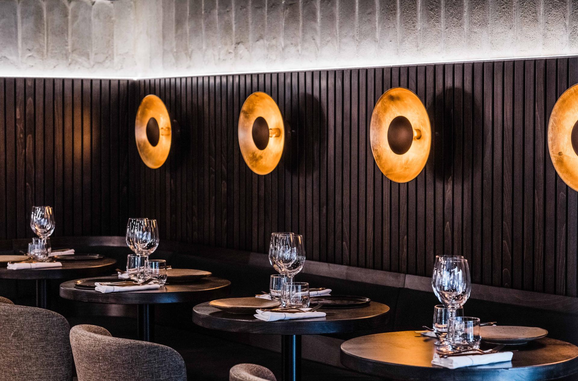 Elegant restaurant interior featuring dark wooden walls, round tables, and contemporary lighting, showcasing TS-DS's design aesthetic.