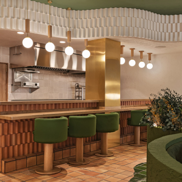 Stylish restaurant interior featuring green seating, vibrant plants, and warm lighting, designed by Masquespacio for Pukkel in Huesca.