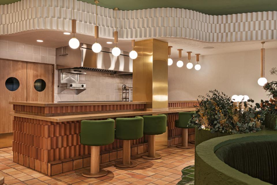 Stylish restaurant interior featuring green seating, vibrant plants, and warm lighting, designed by Masquespacio for Pukkel in Huesca.