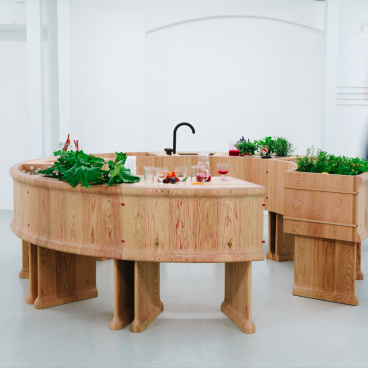 Curved red oak bar with plants and drinks, designed by Chan + Eayrs and Sebastian Cox for Milan Design Week.
