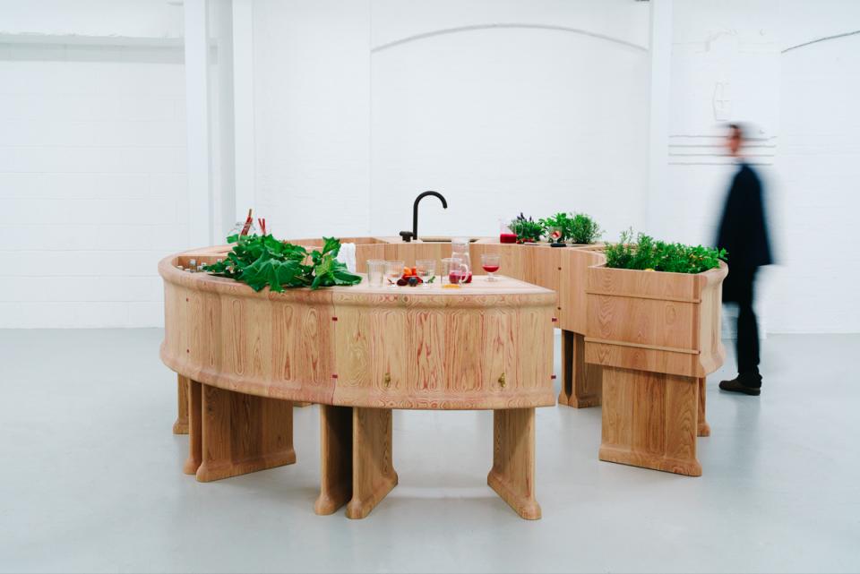 Curved red oak bar with plants and drinks, designed by Chan + Eayrs and Sebastian Cox for Milan Design Week.