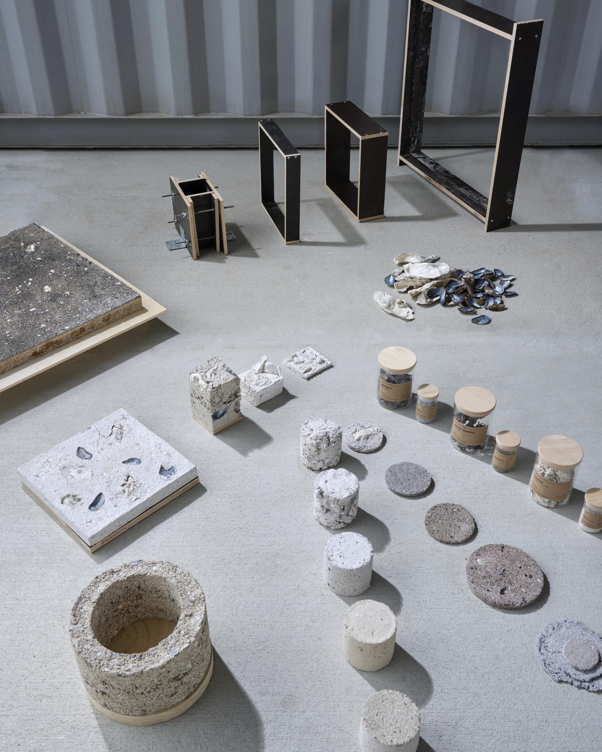 Various innovative biomaterial samples and waste-based products arranged on a concrete surface, showcasing sustainable design in 2025.