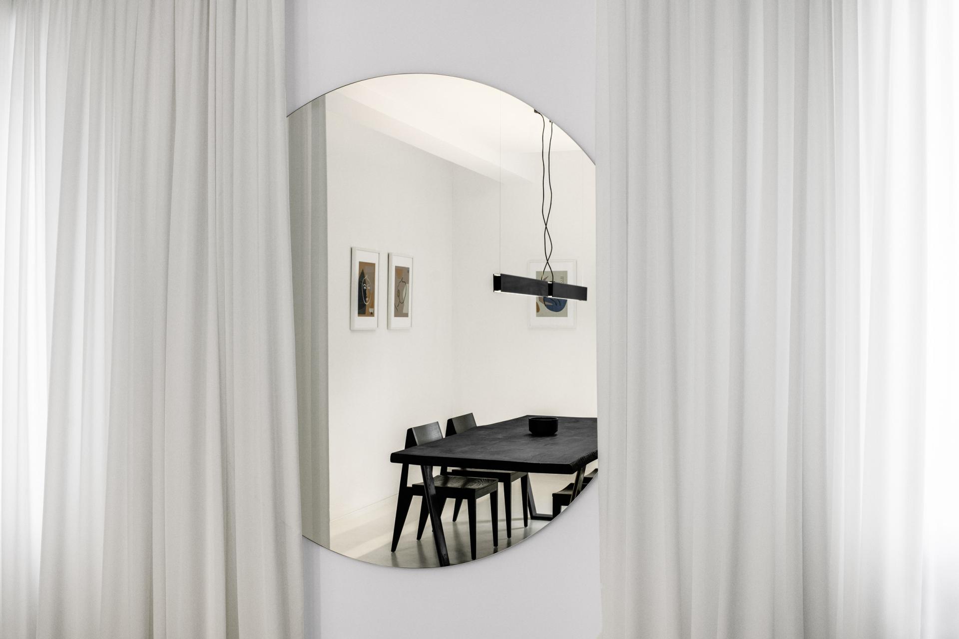 Modern interior design featuring a circular mirror reflecting a black dining table and minimalist decor in a stylish atelier.