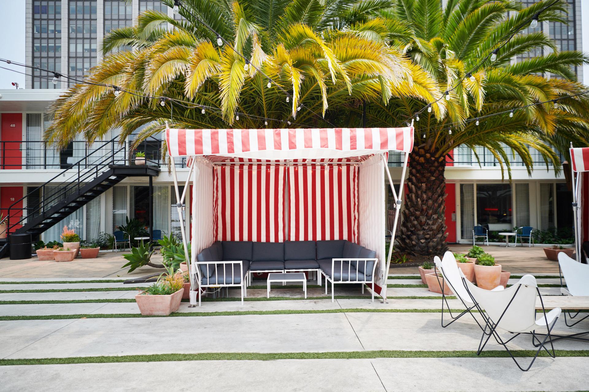 Renovated outdoor seating area at the Phoenix Hotel, featuring a striped cabana and palm trees in San Francisco.