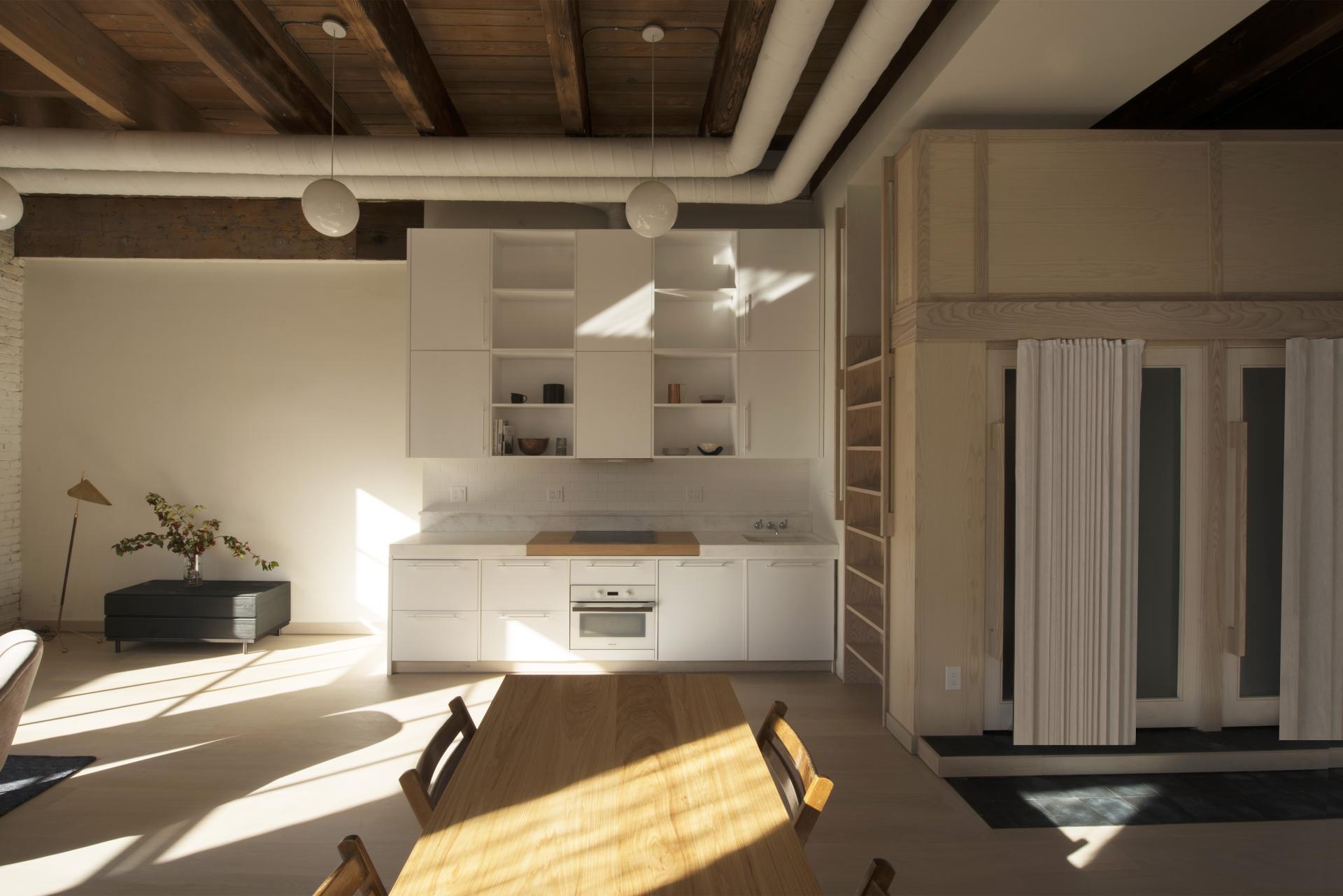 Bright and modern loft kitchen designed by Corey Kingston, featuring minimalist cabinetry, a dining table, and open space.