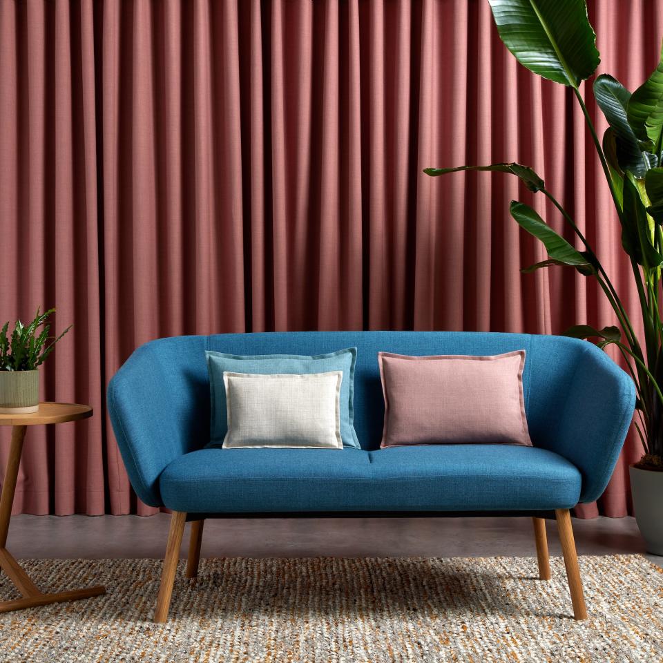 Vibrant blue sofa adorned with pastel cushions, set against textured curtains, showcasing Camira's latest Sumi fabric colors.