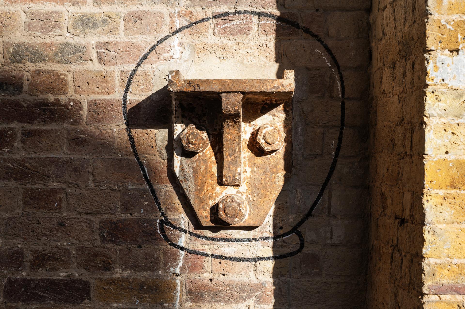 Rusty metal fixture with abstract face outline on a brick wall at Borough Yards, London’s cultural destination.